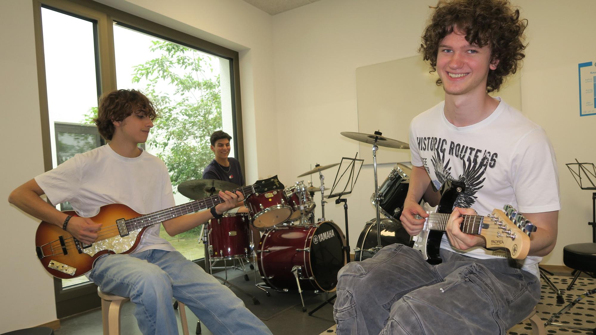 Drei junge Männer sitzen mit ihren Instrumenten in einem Proberaum.