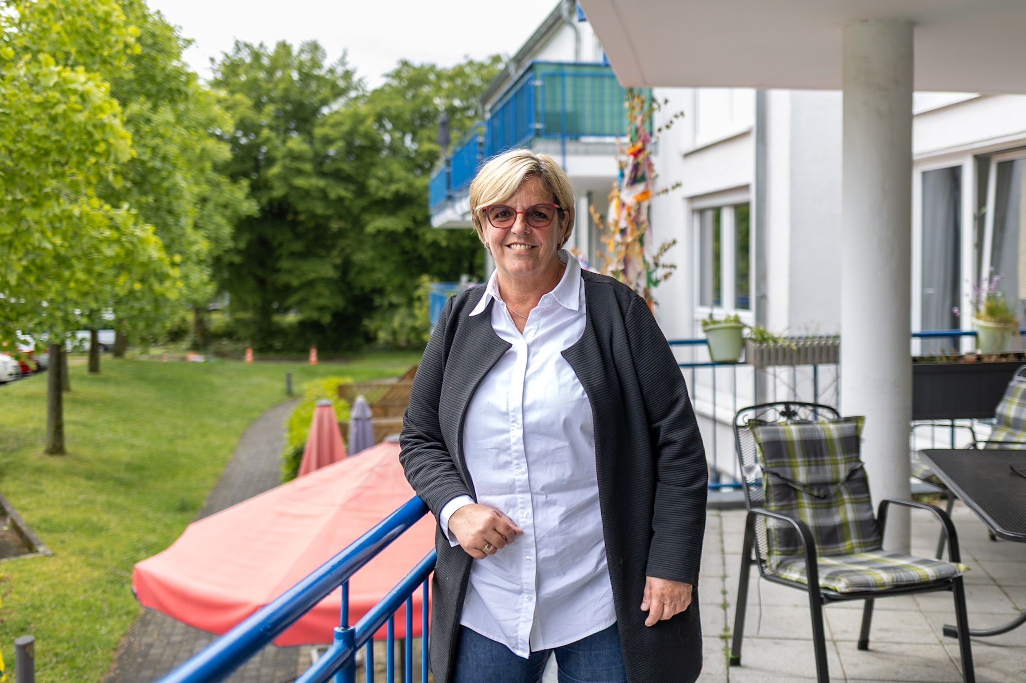 Eine Frau mit Brille steht auf einem großen Balkon.