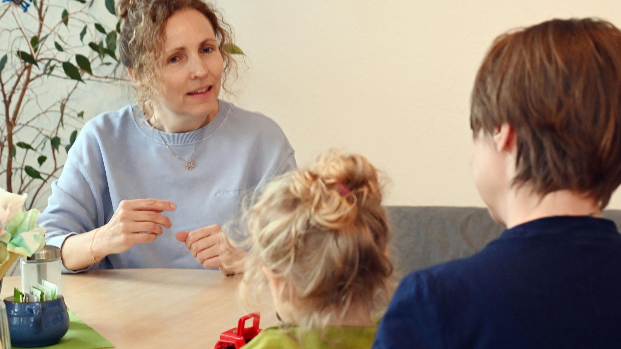Eine Frau mit Locken sitzt einer Mutter gegenüber, die ein blondgelocktes Kind auf dem Schoß hat.