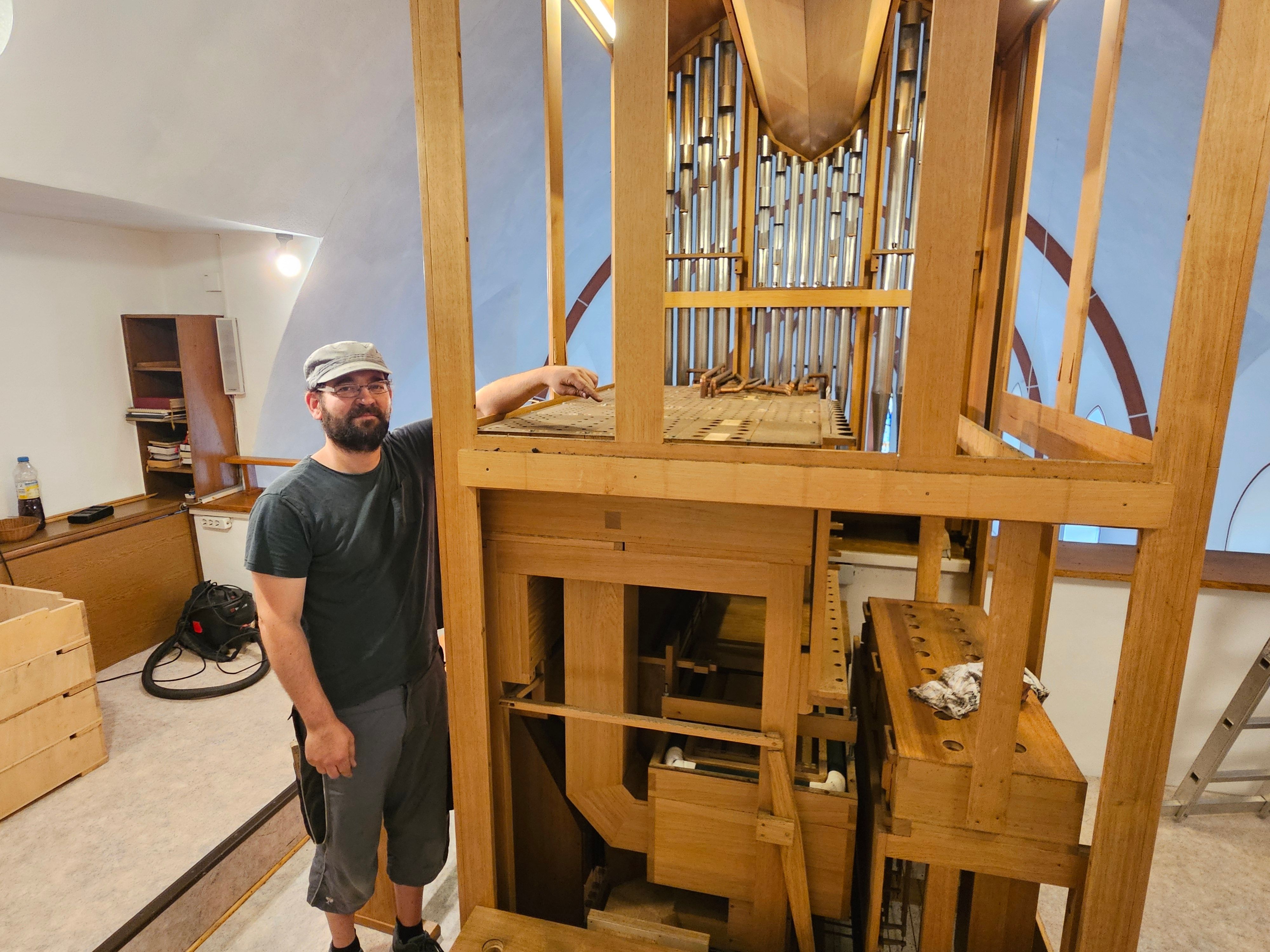 Ein Mann mit Kappe steht neben einer Orgel.