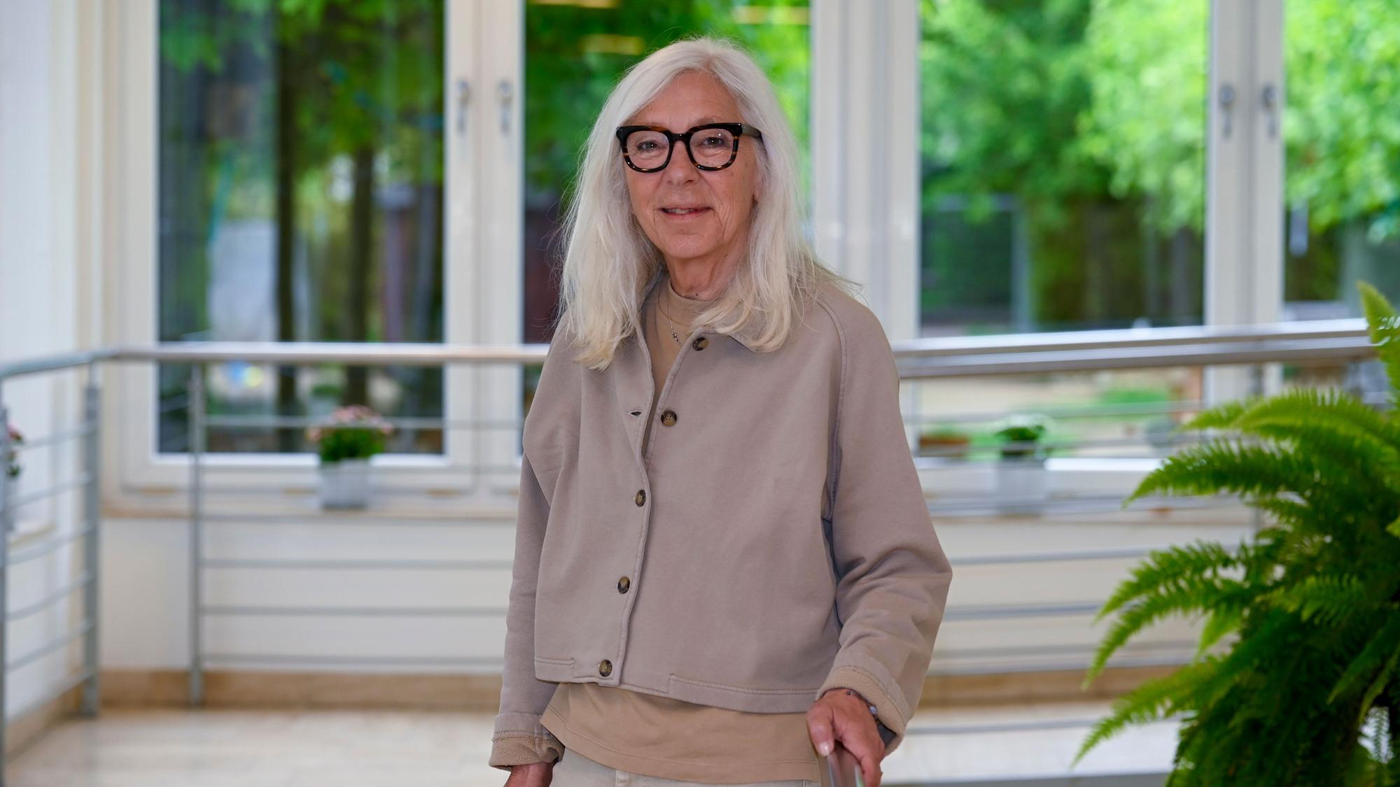 Eine Frau mit weißen Haaren und Brille lächelt in die Kamera.