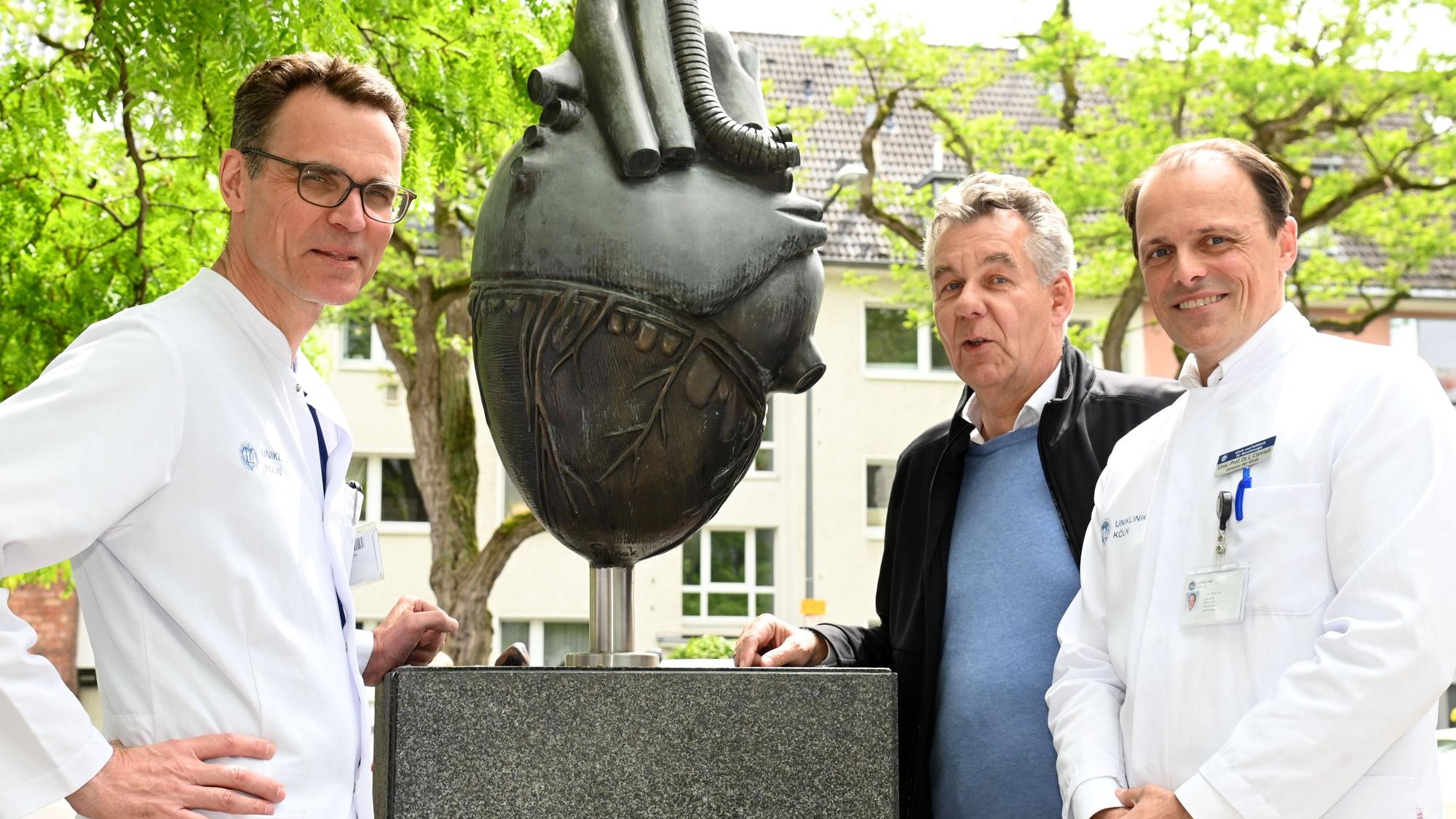 Peter Wessling (Mitte) vor der Kölner Uniklinik mit Herzskulptur und den Herzspezialisten Stephan Baldus (l.) und Lenard Conradi.