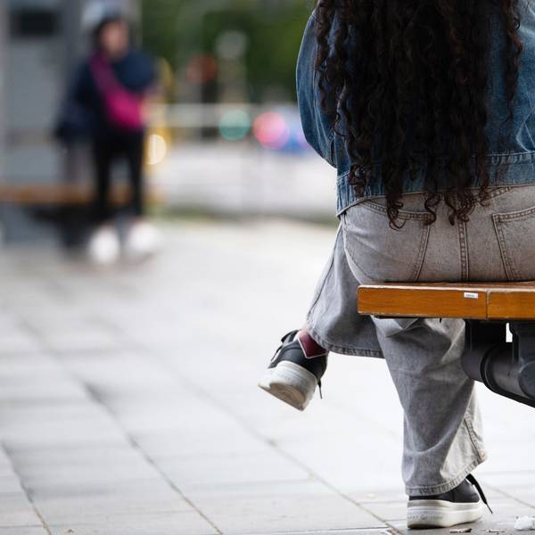 Eine junge Frau sitzt an einer Haltestelle auf einer Bank