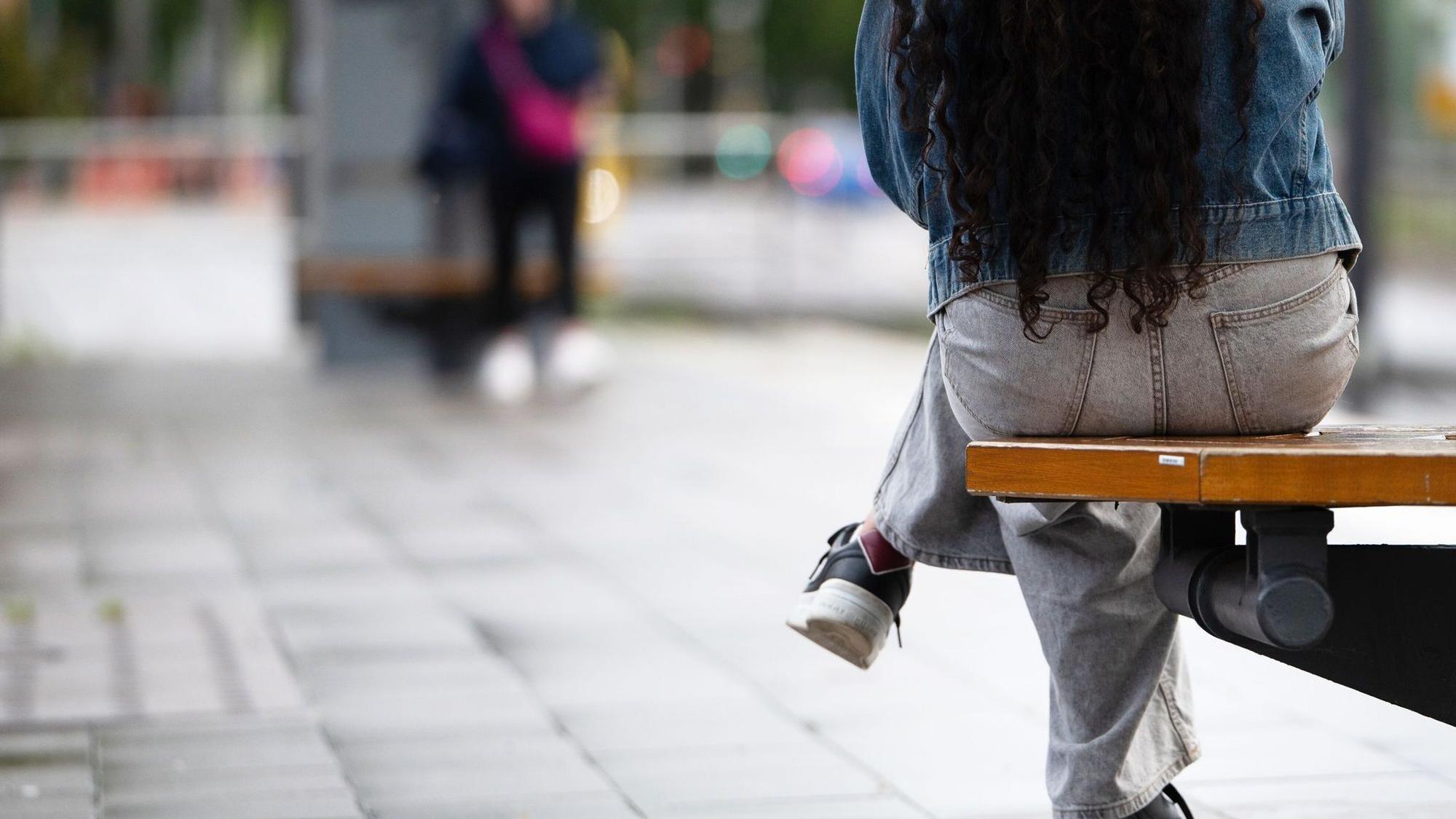 Eine junge Frau sitzt an einer Haltestelle auf einer Bank