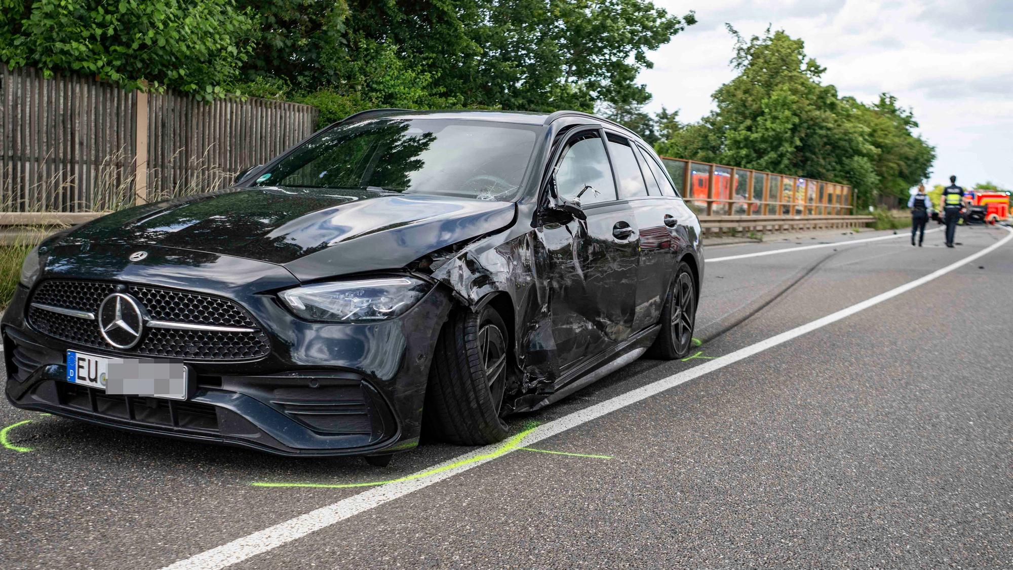 Das Bild zeigt einen schwarzen Mercedes, der im Bereich der Fahrerseite beschädigt ist.