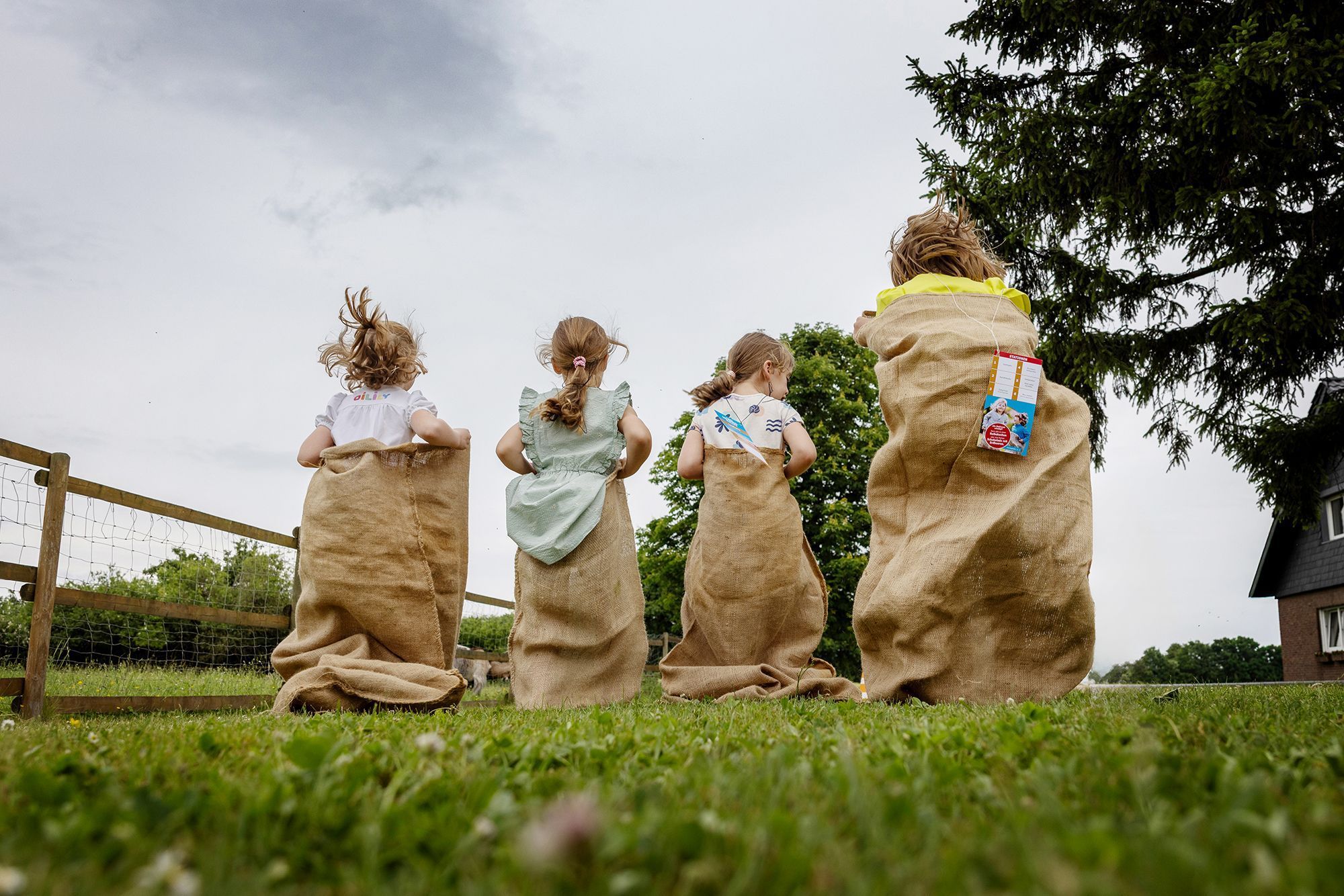 Vier Kinder in Säcken hüpfen über eine Wiese.