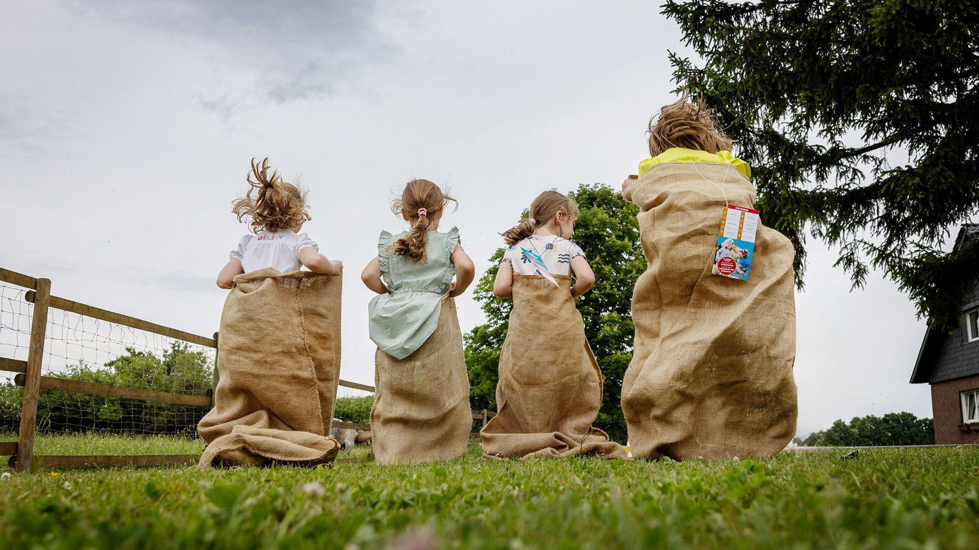 Vier Kinder in Säcken hüpfen über eine Wiese.