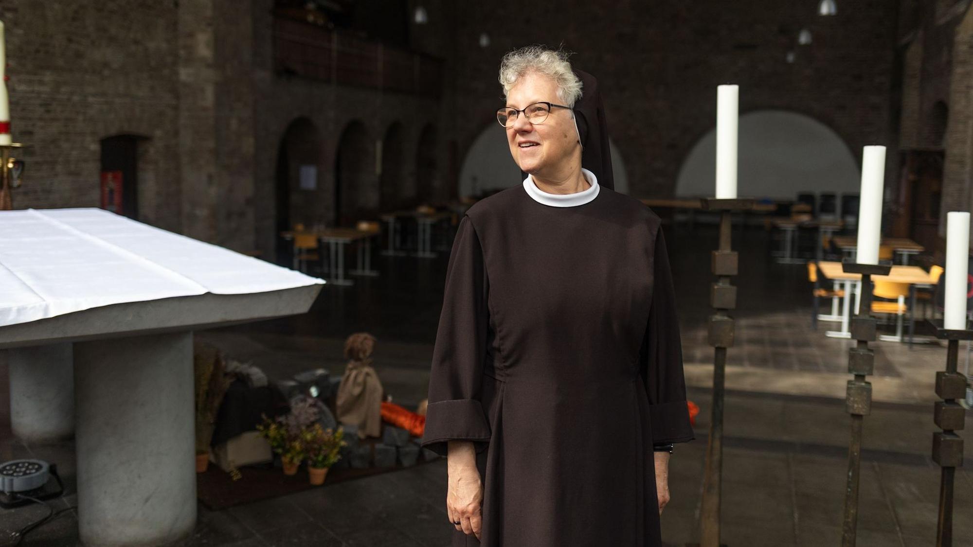 Eine Frau in schwarzer Nonnenkleidung steht in einer Kirche.