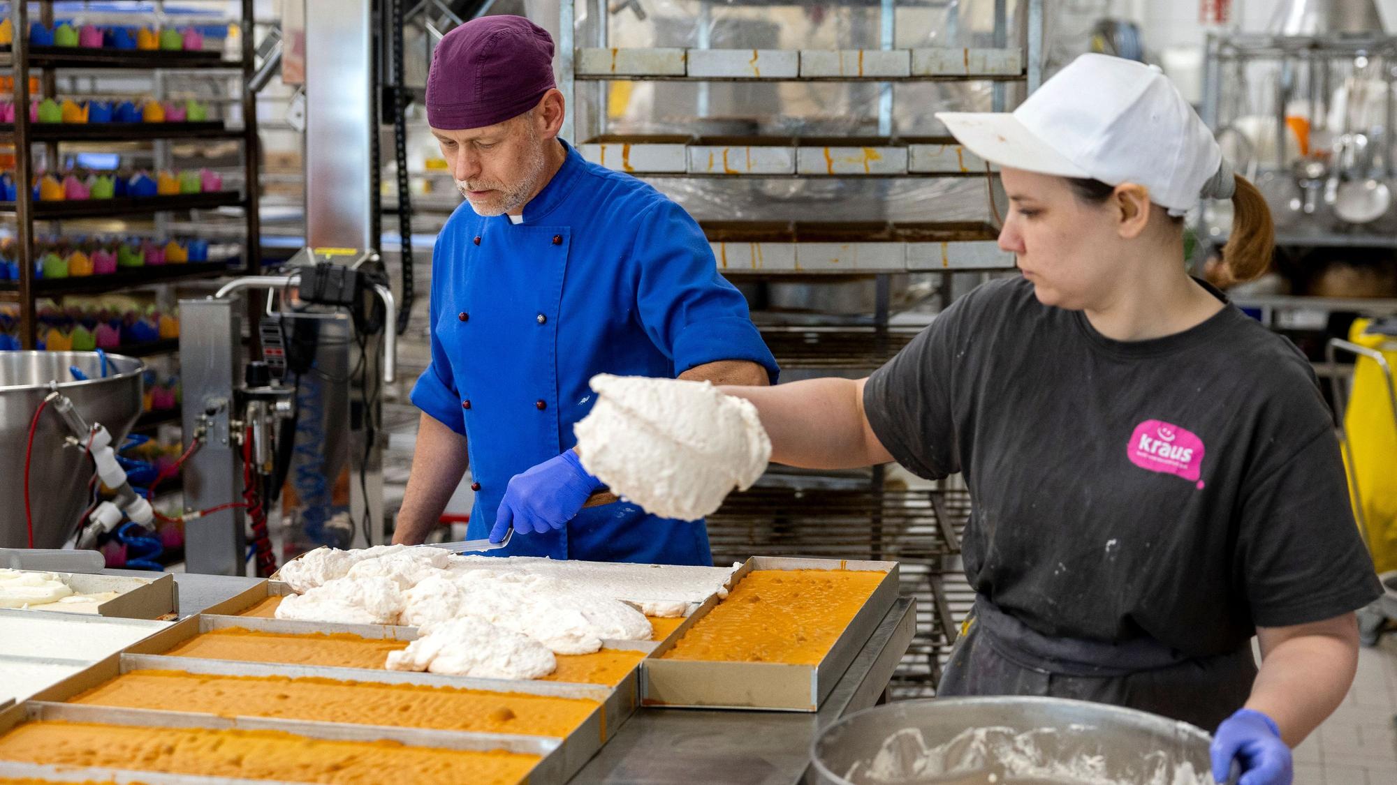Zwei Mitarbeitende belegen Kuchenböden in eckigen Formen mit einer Sahnemasse.