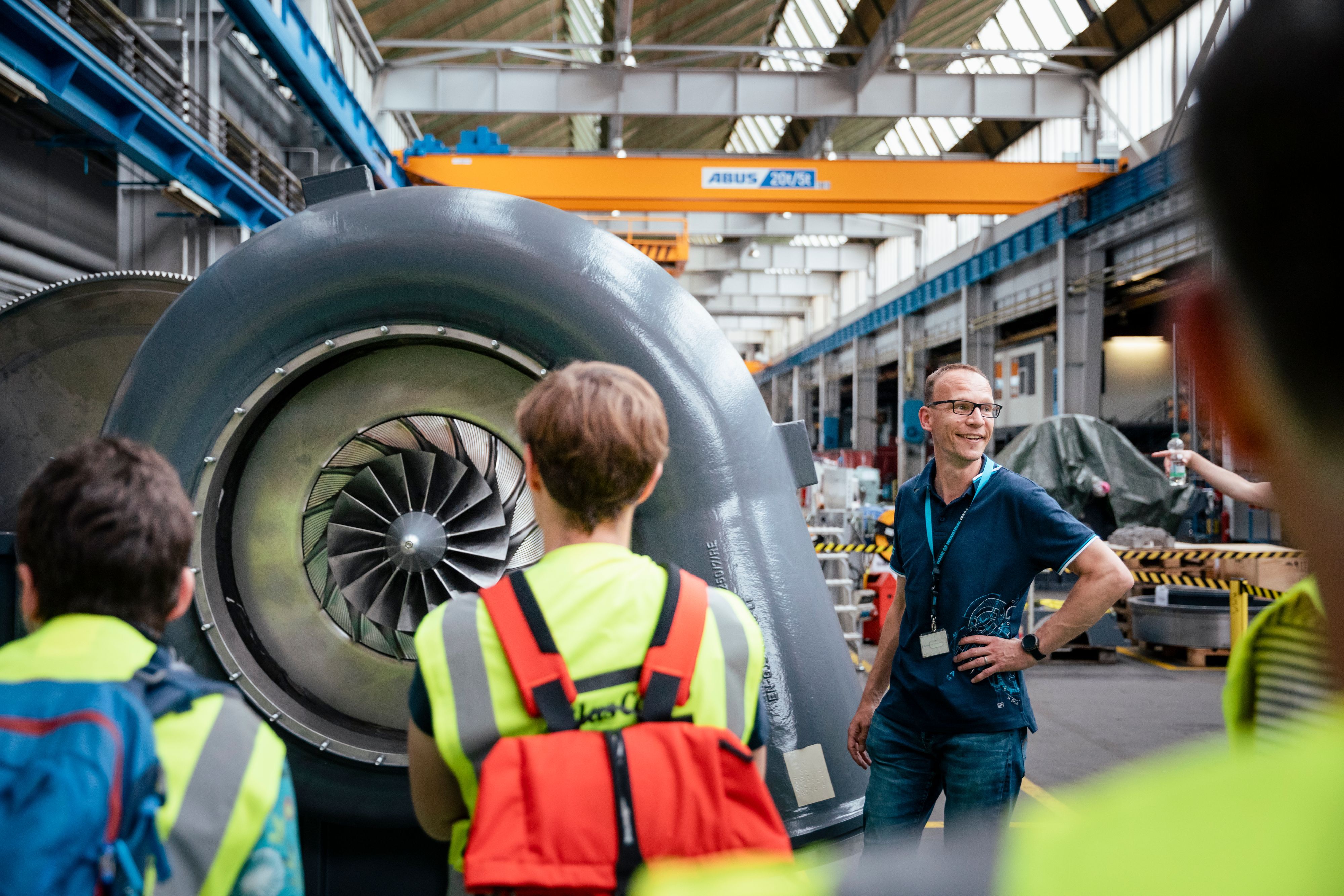 Besucher stehen in einem Industriebetrieb vor einer Turbine.