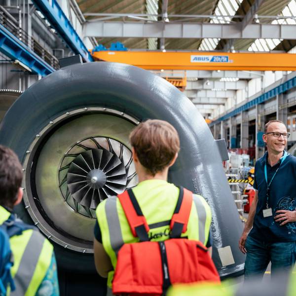 Besucher stehen in einem Industriebetrieb vor einer Turbine.