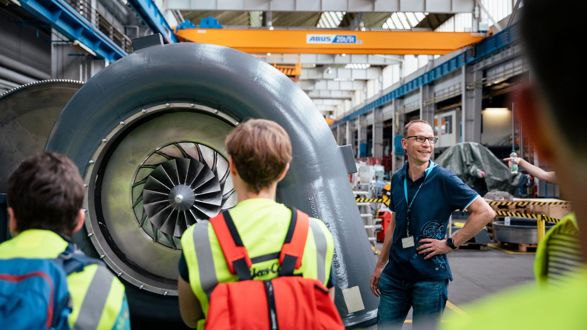 Besucher stehen in einem Industriebetrieb vor einer Turbine.