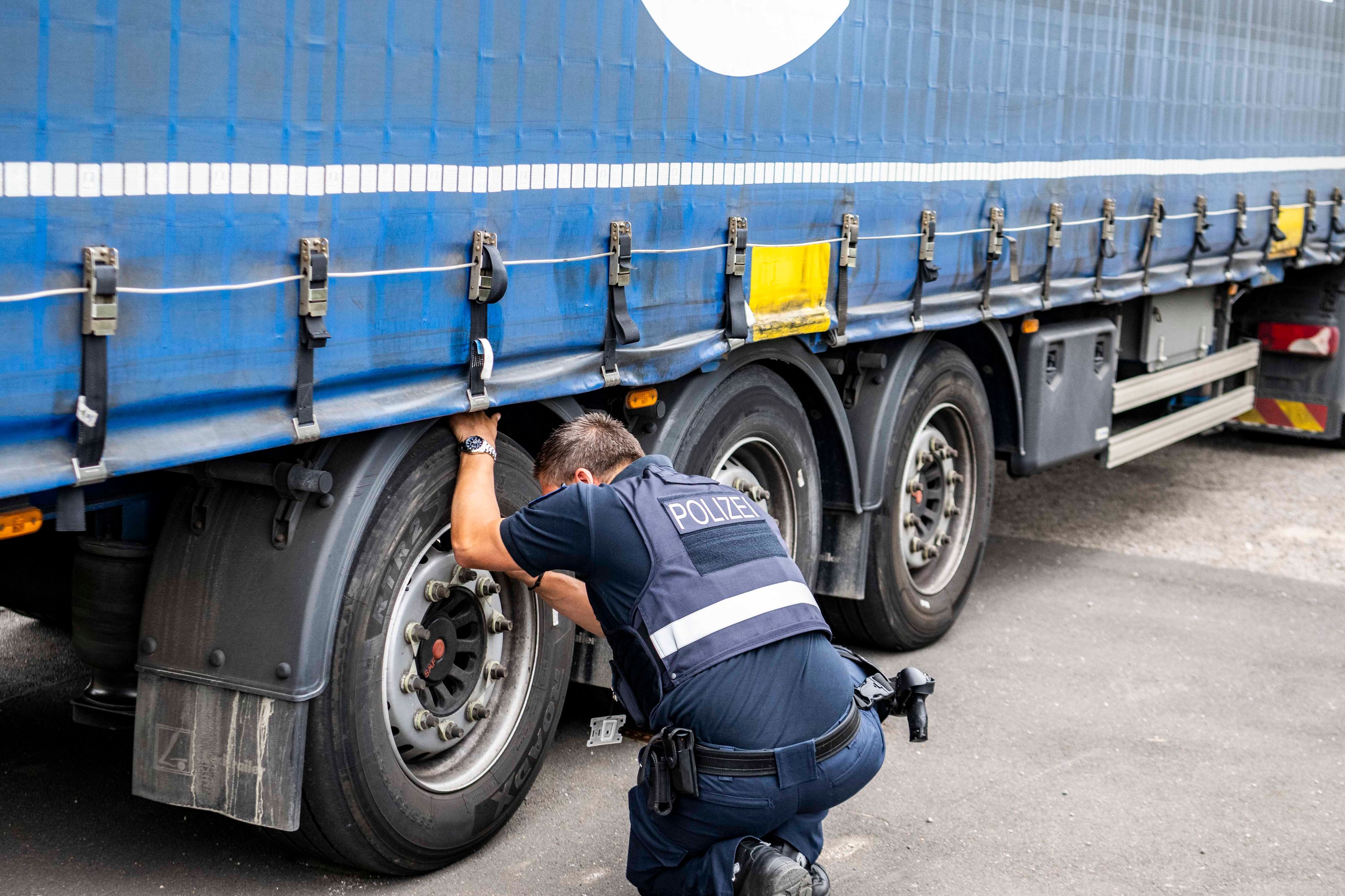 Das Bild zeigt einen Polizisten, der sich die Reifen eines Sattelschleppers genau anschaut.