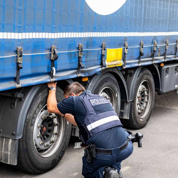 Das Bild zeigt einen Polizisten, der sich die Reifen eines Sattelschleppers genau anschaut.
