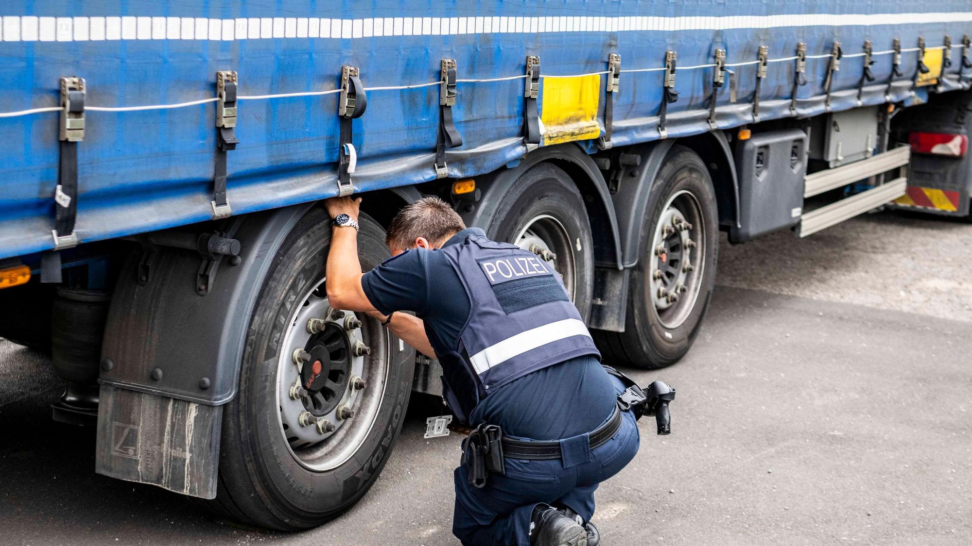 Das Bild zeigt einen Polizisten, der sich die Reifen eines Sattelschleppers genau anschaut.