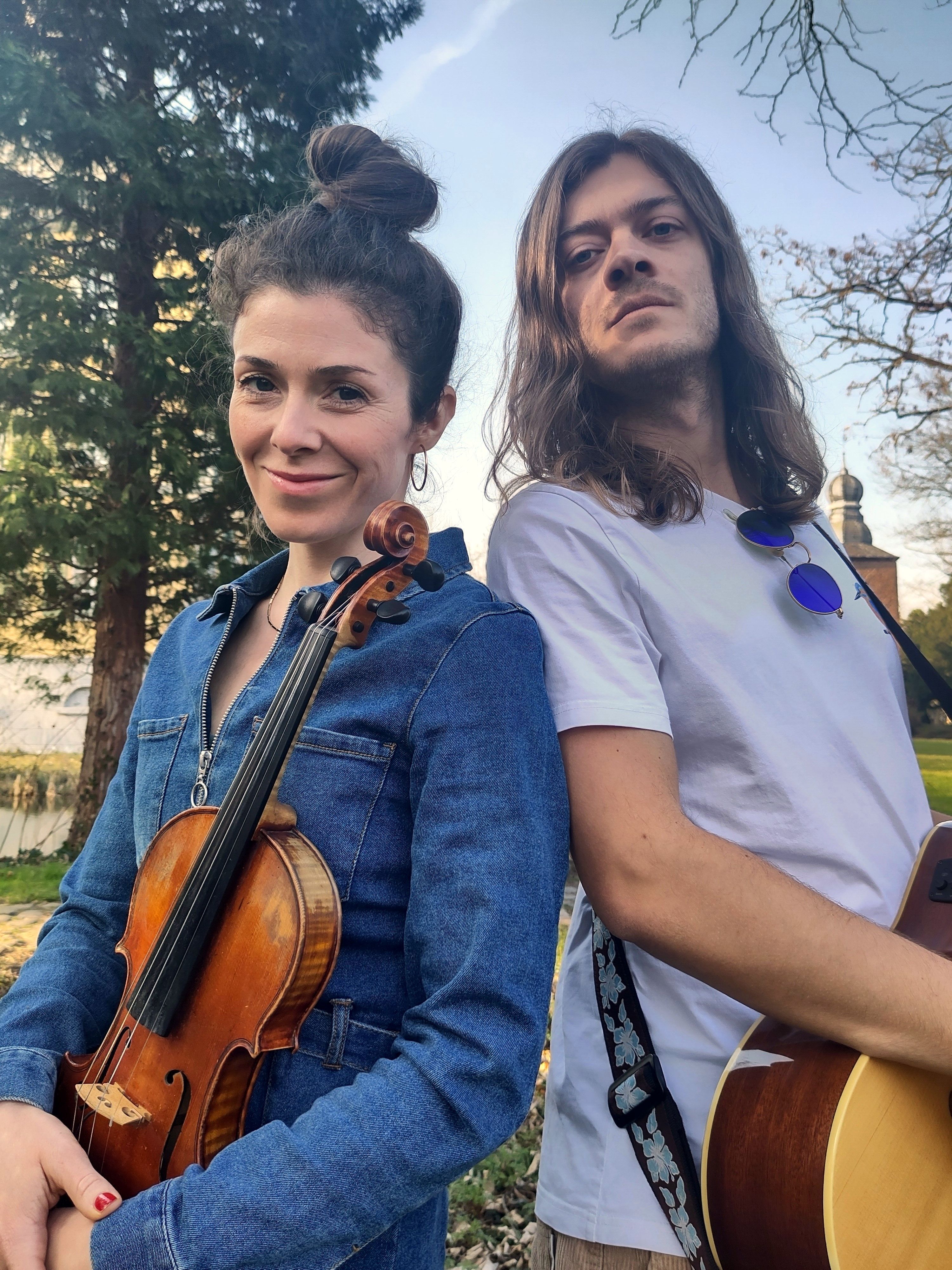 Alisha hält eine Geige in der Hand, J. Low hat eine Gitarre umhängen.