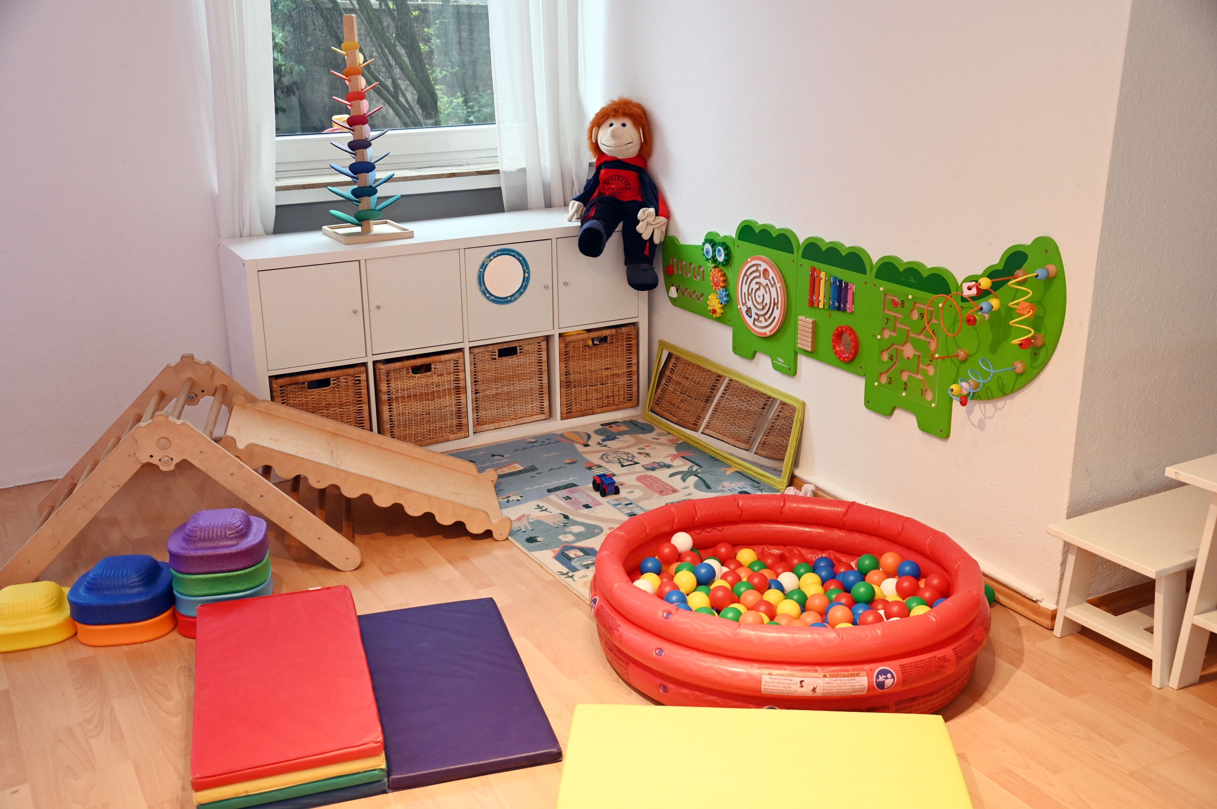 In einer Ecke eines Raumes stehen eine kleine Rutsche, ein Bällebad, Wandspiele und Turnmatten.