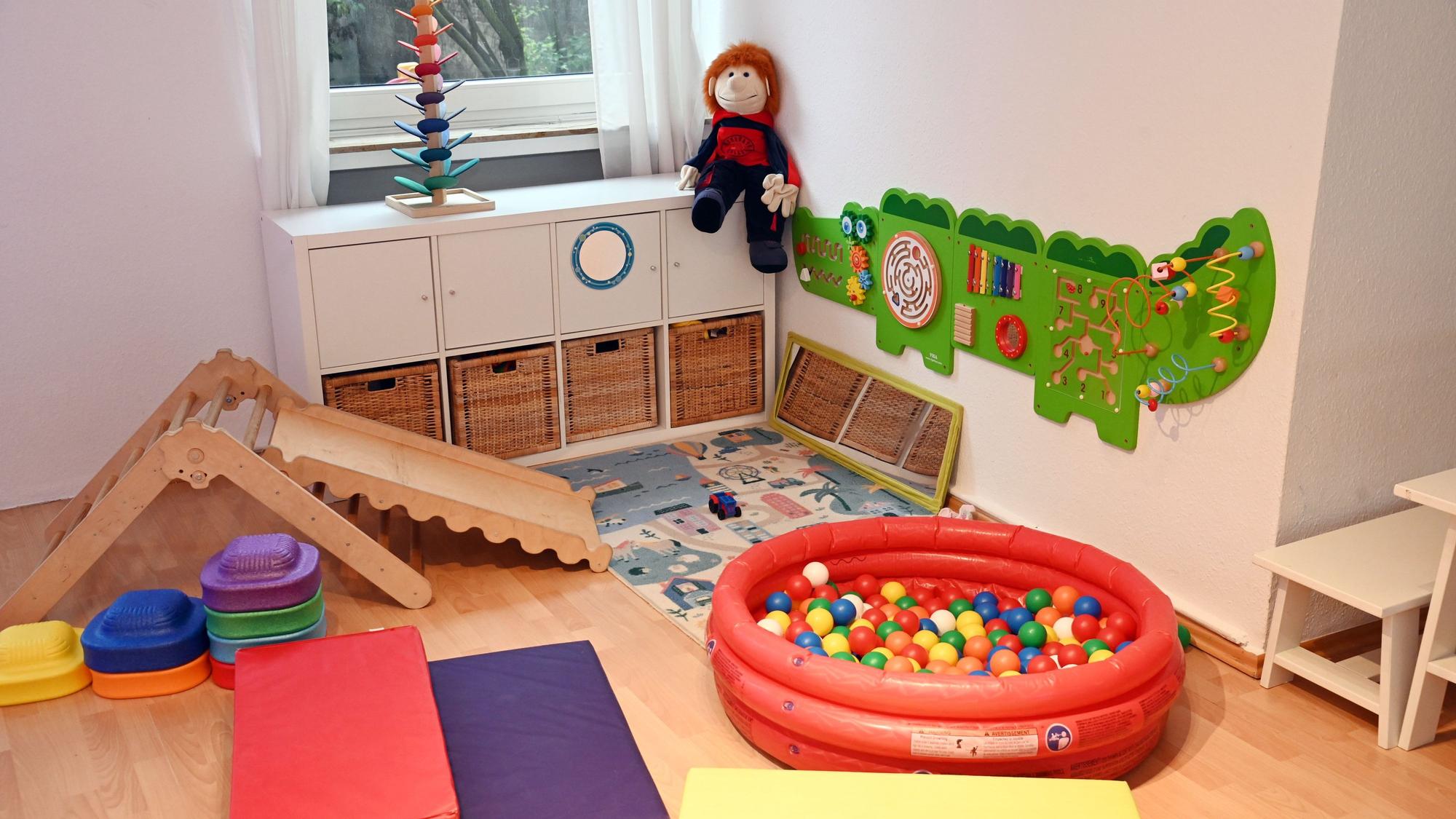 In einer Ecke eines Raumes stehen eine kleine Rutsche, ein Bällebad, Wandspiele und Turnmatten.