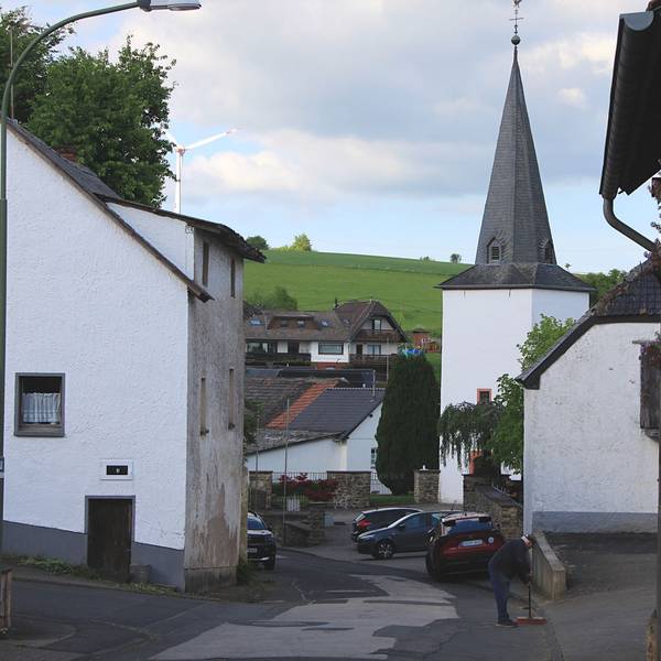 Das Foto zeigt die Kirche in Reetz, drumherum stehen Häuser, auf einem Hügel steht ein Windrad.