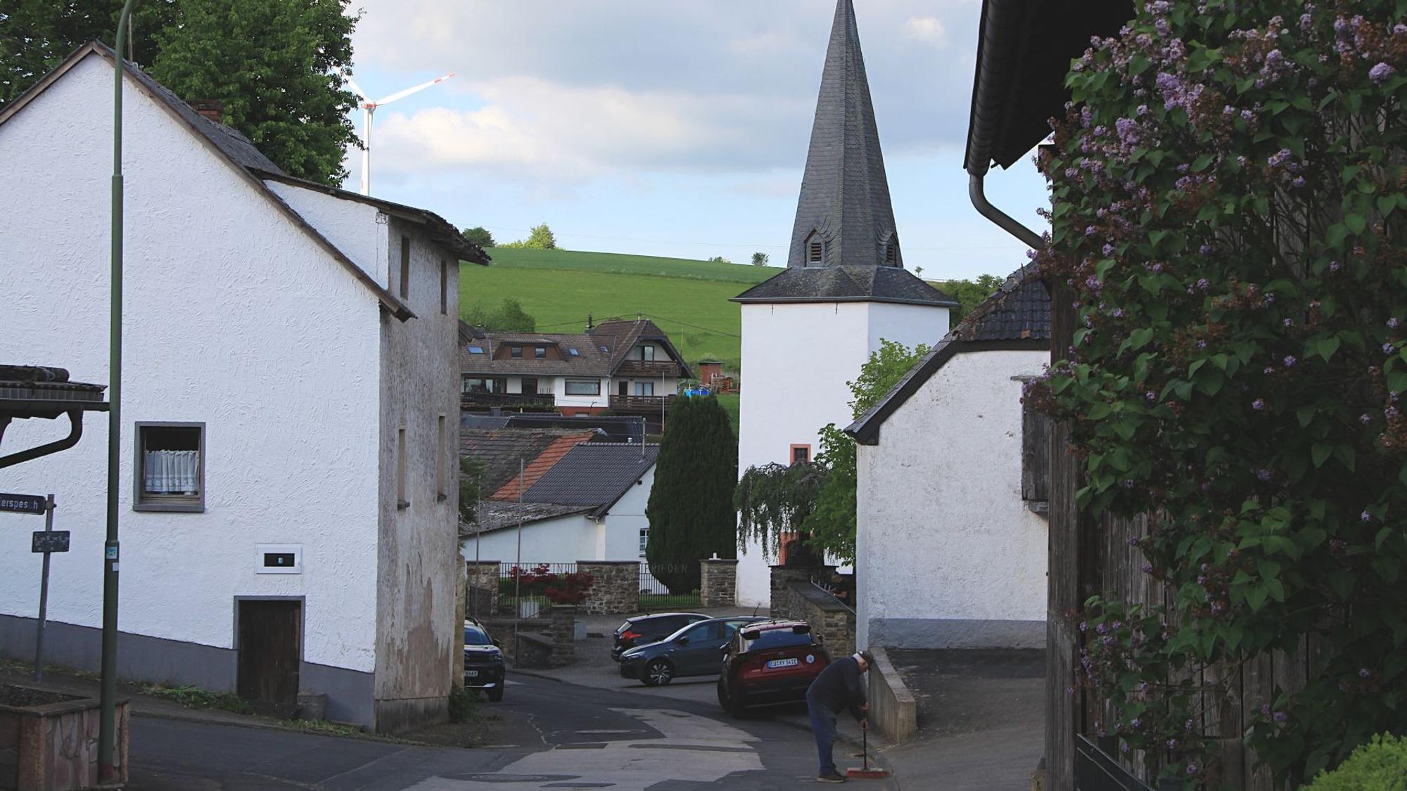 Das Foto zeigt die Kirche in Reetz, drumherum stehen Häuser, auf einem Hügel steht ein Windrad.