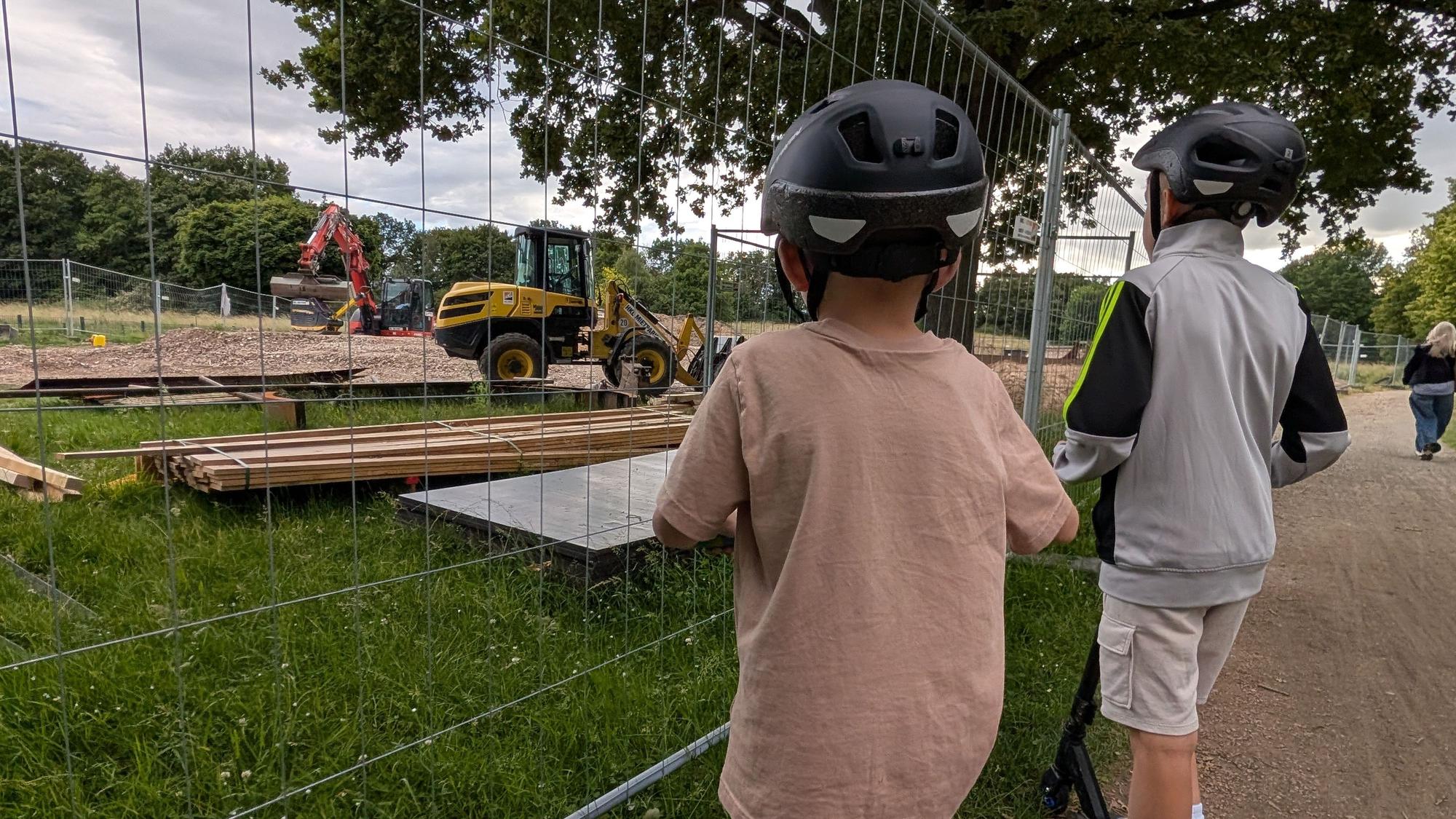 Das Foto zeigt zwei Jungen, die durch den Bauzaun auf die Baustelle der Skateanlage im Bürgerpark schauen.