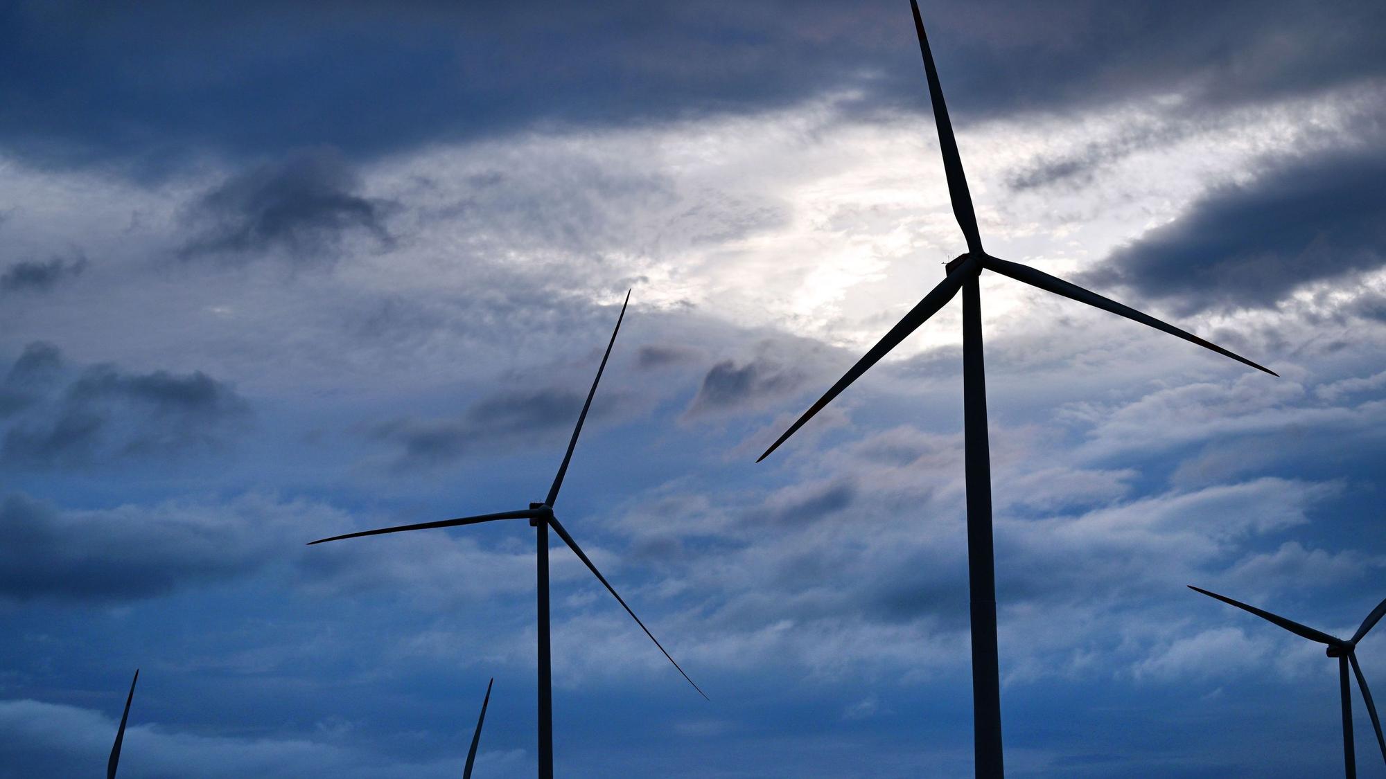 Über einem Windpark bei Gotha scheint Sonnenlicht zwischen dunklen Regenwolken hindurch.