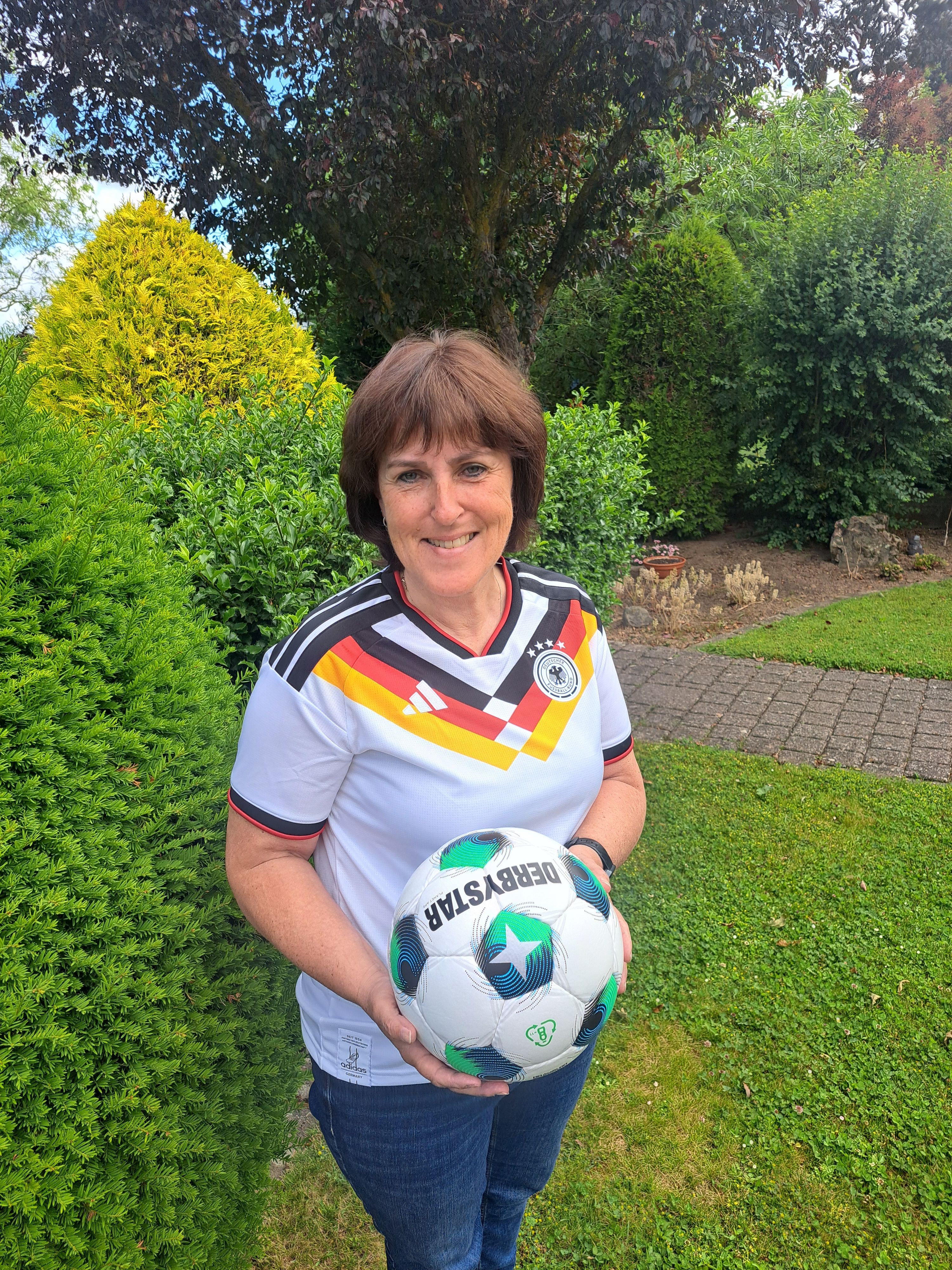 Doris Mager trägt das aktuelle WM-Trikot und hält einen Fußball in der Hand.