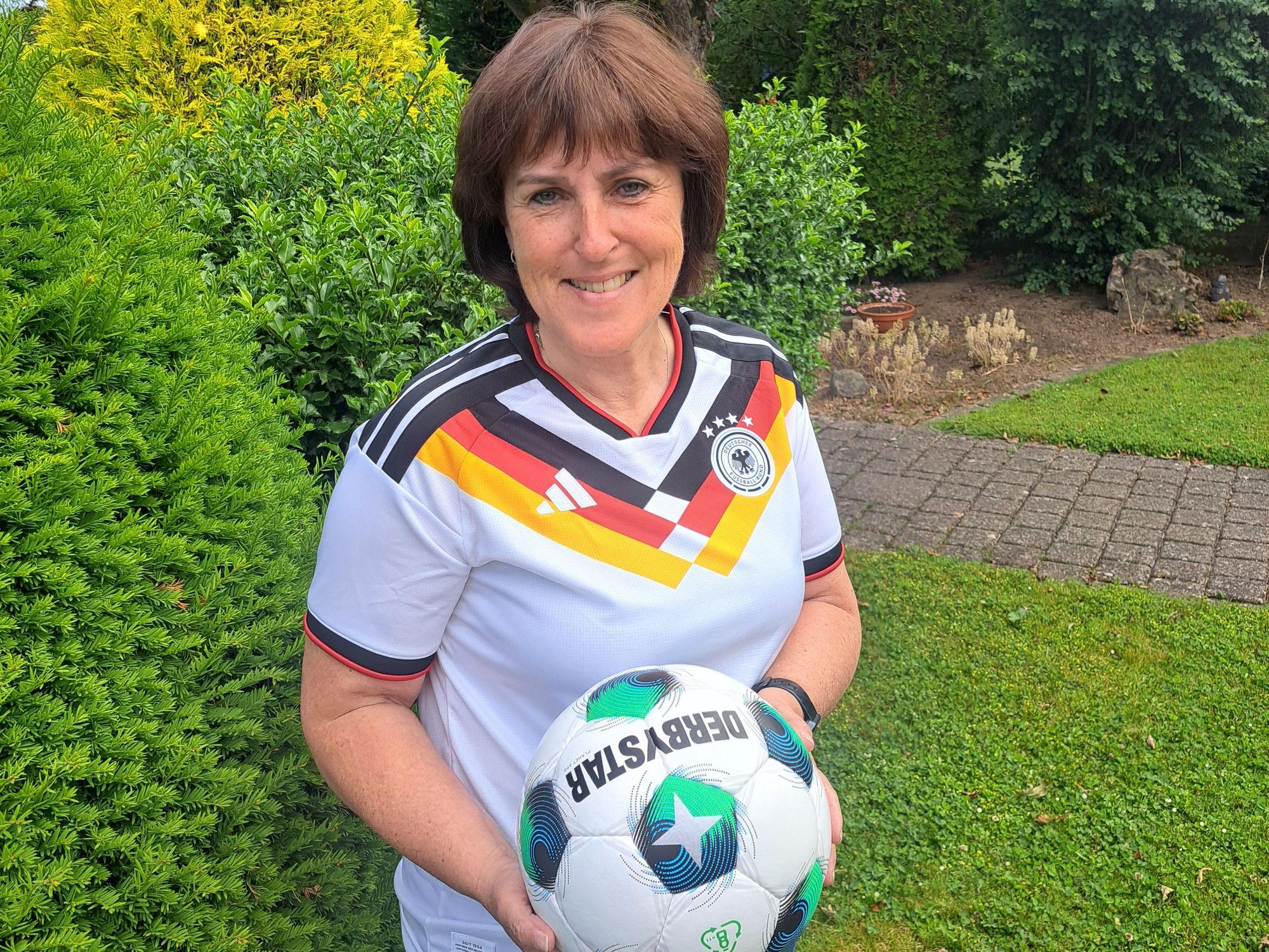 Doris Mager trägt das aktuelle WM-Trikot und hält einen Fußball in der Hand.