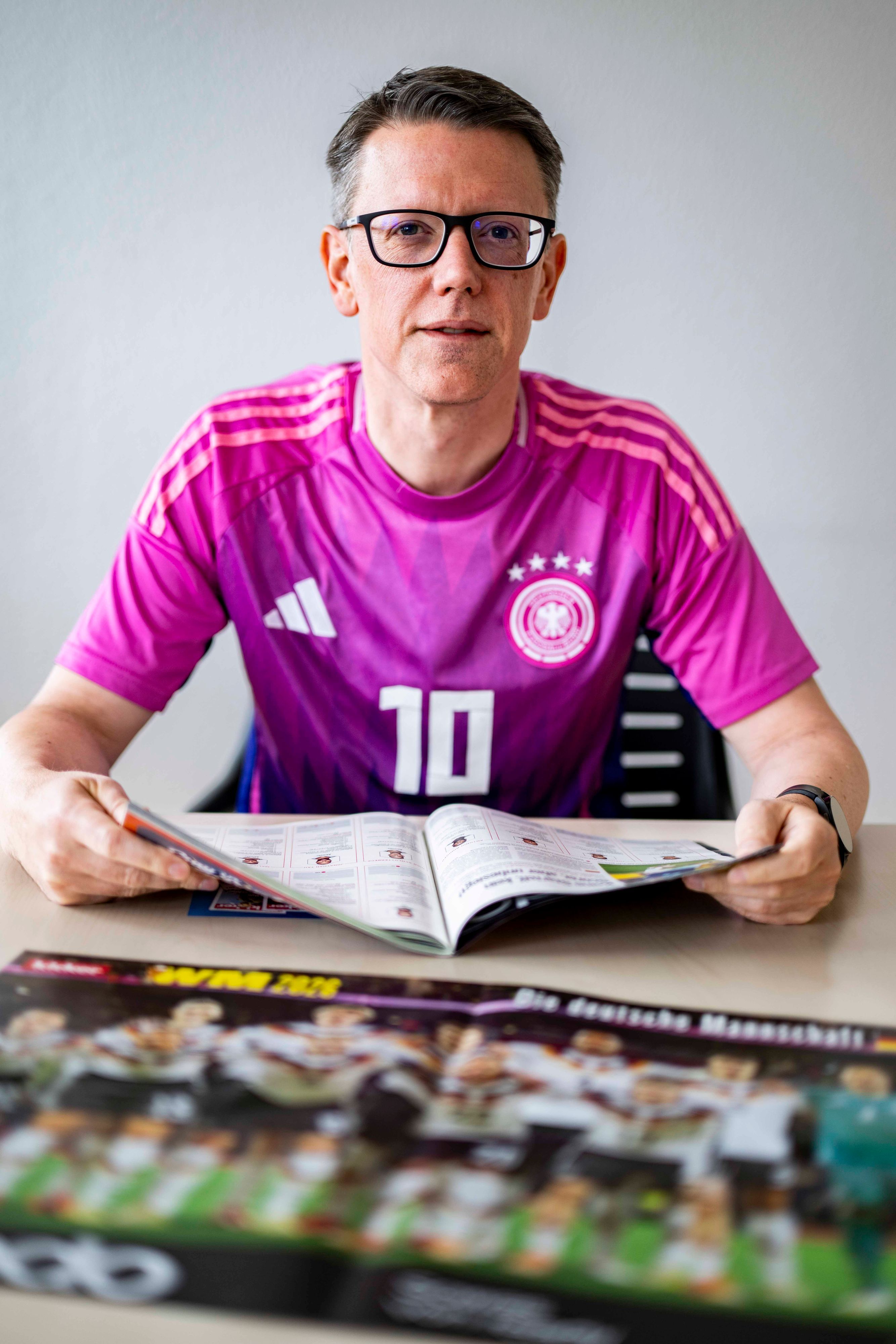 Thomas Schmitz sitzt im deutschen Auswärtstrikot der WM 2022 am Tisch und blättert im Kicker-Sonderheft.