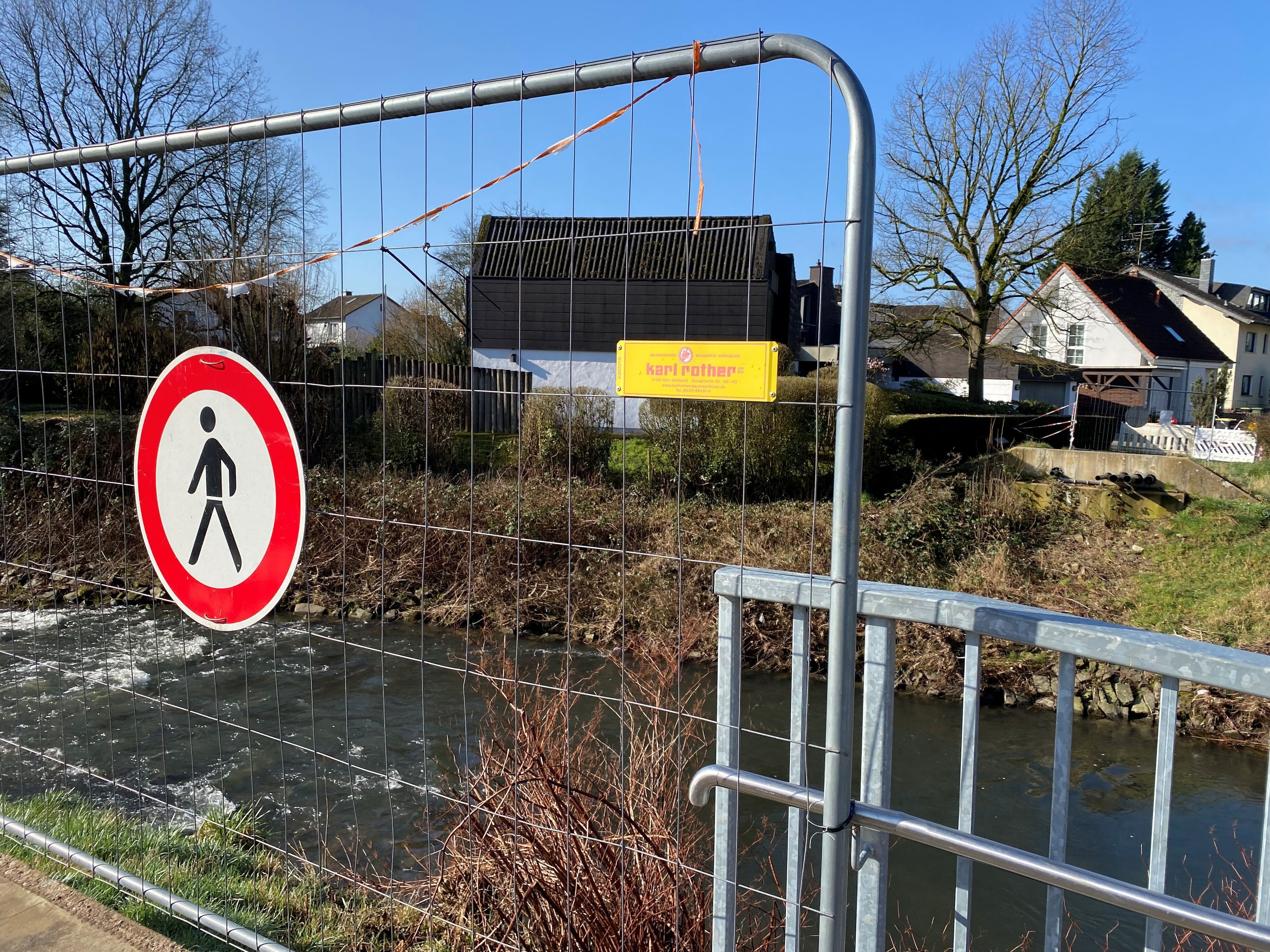 Eine Absperrung für Fußgänger, dahinter ein Fluss, am anderen Ufer kann man Betonreste sehen von der abgerissenen Mauer