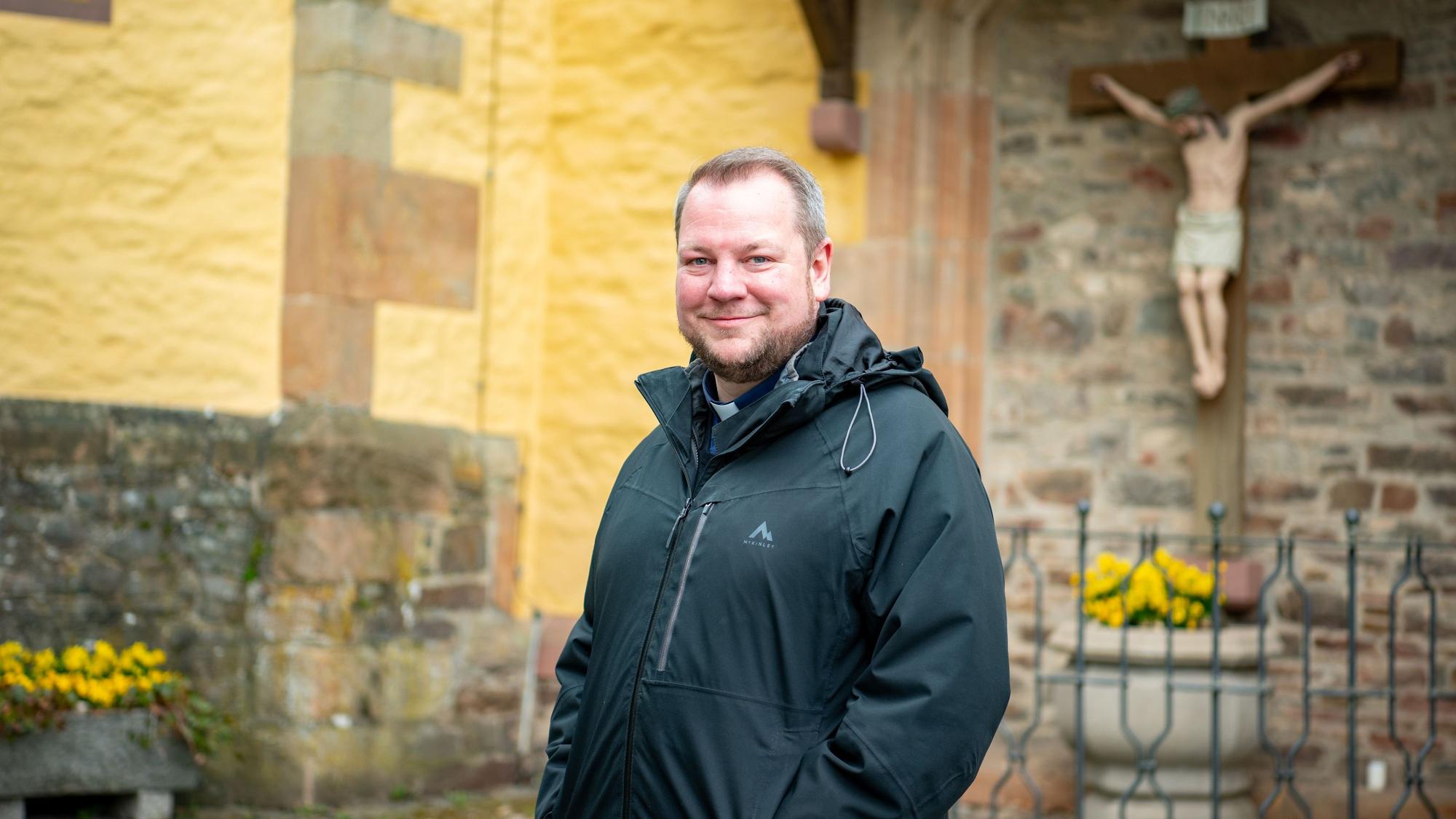 Pfarrer Thomas Schlütter steht in schwarzer Regenjacke vor der Schlosskirche in Schleiden.