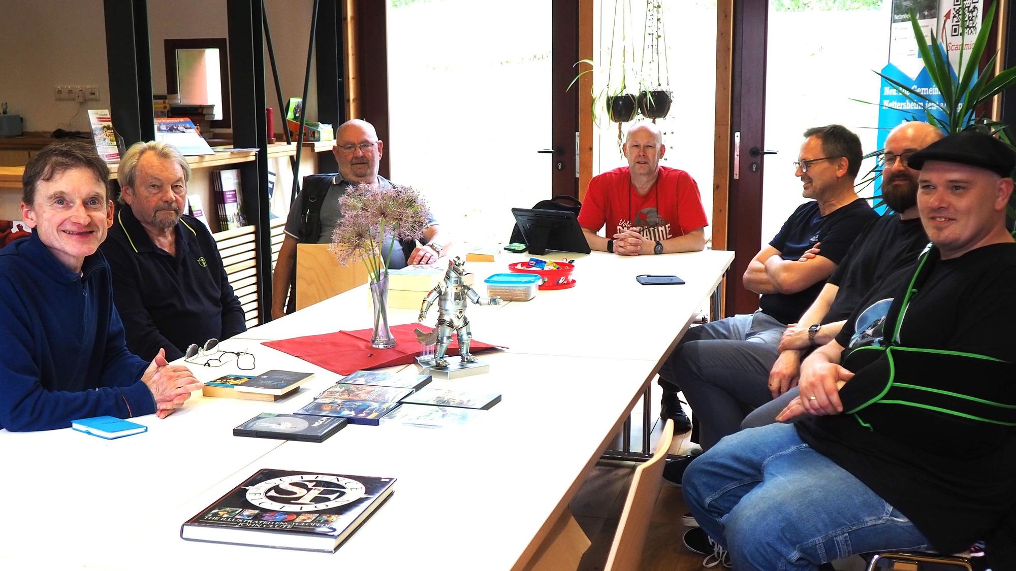 Sieben Männer sitzen an Tischen.