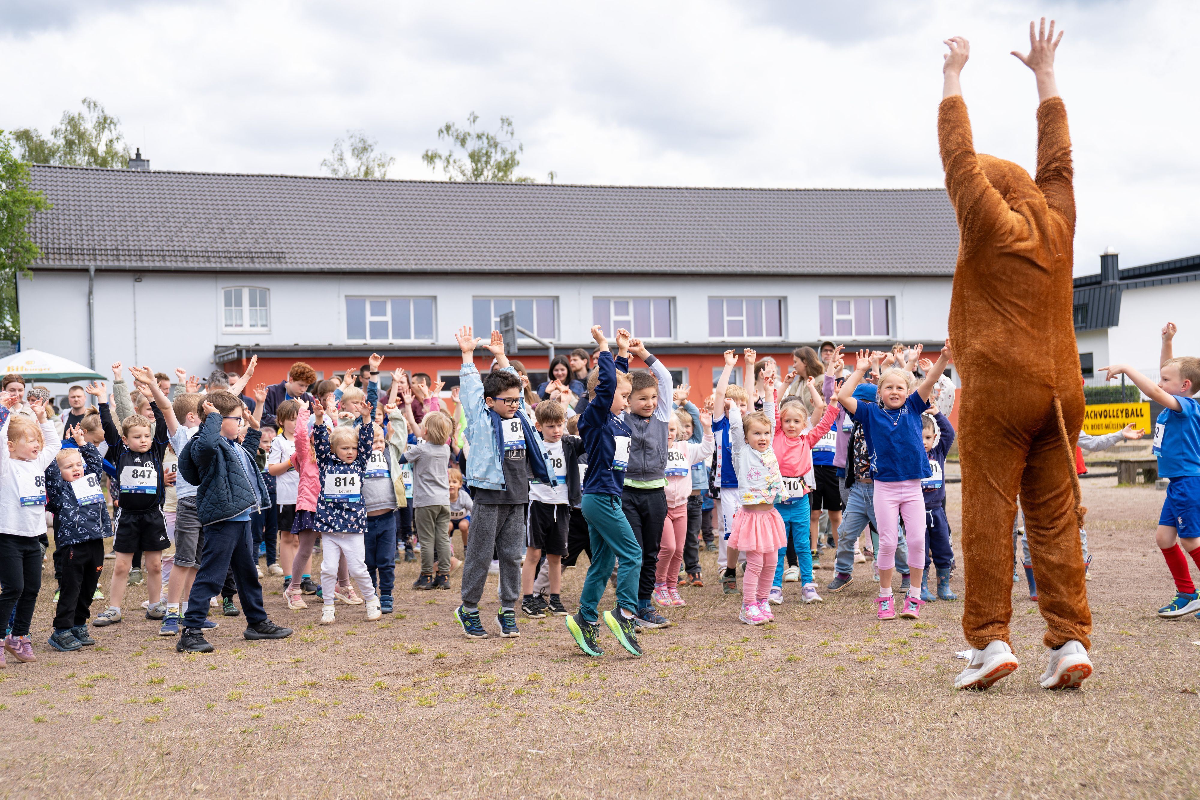 Kinder machen sich vor einem Lauf mit einem Maskottchen im Pferdekostüm warm.