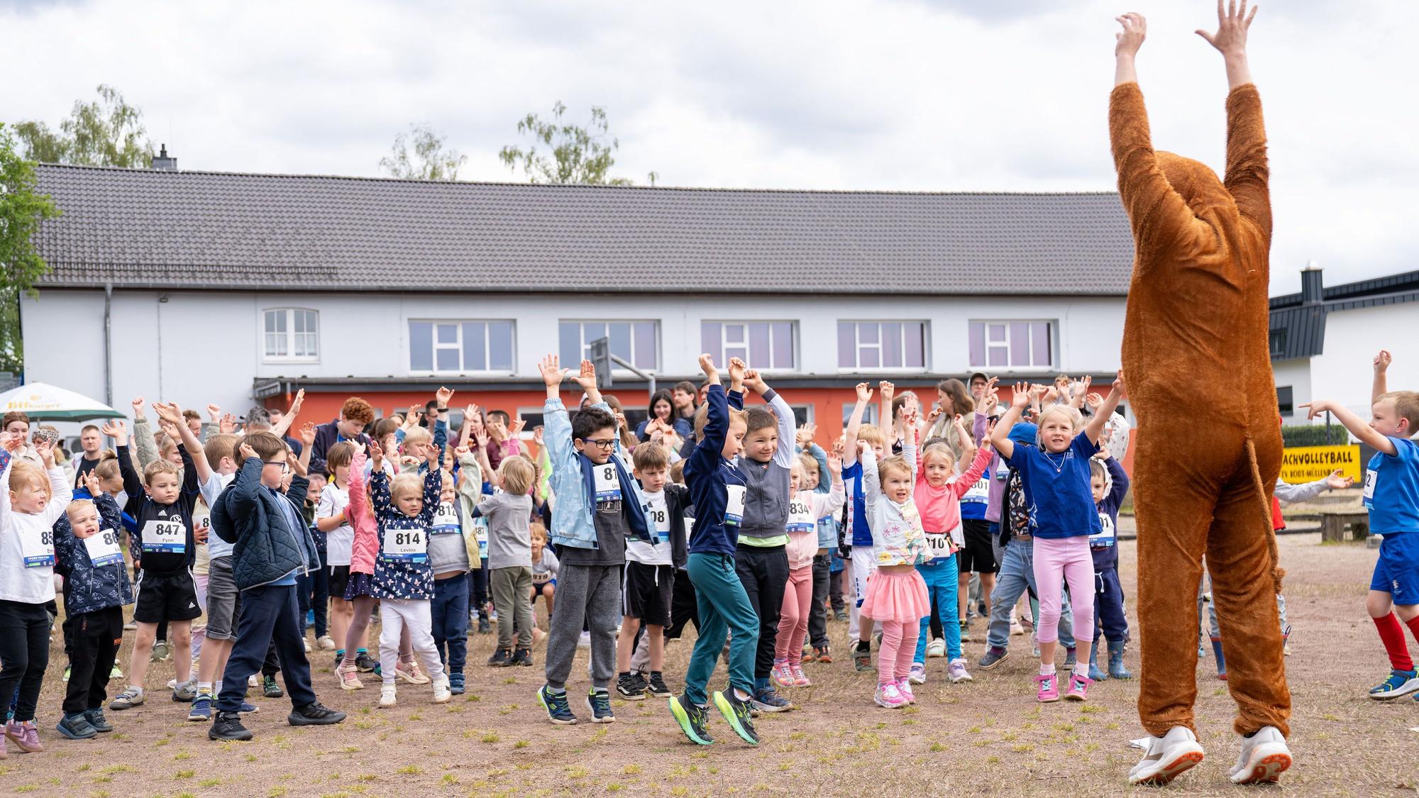 Kinder machen sich vor einem Lauf mit einem Maskottchen im Pferdekostüm warm.