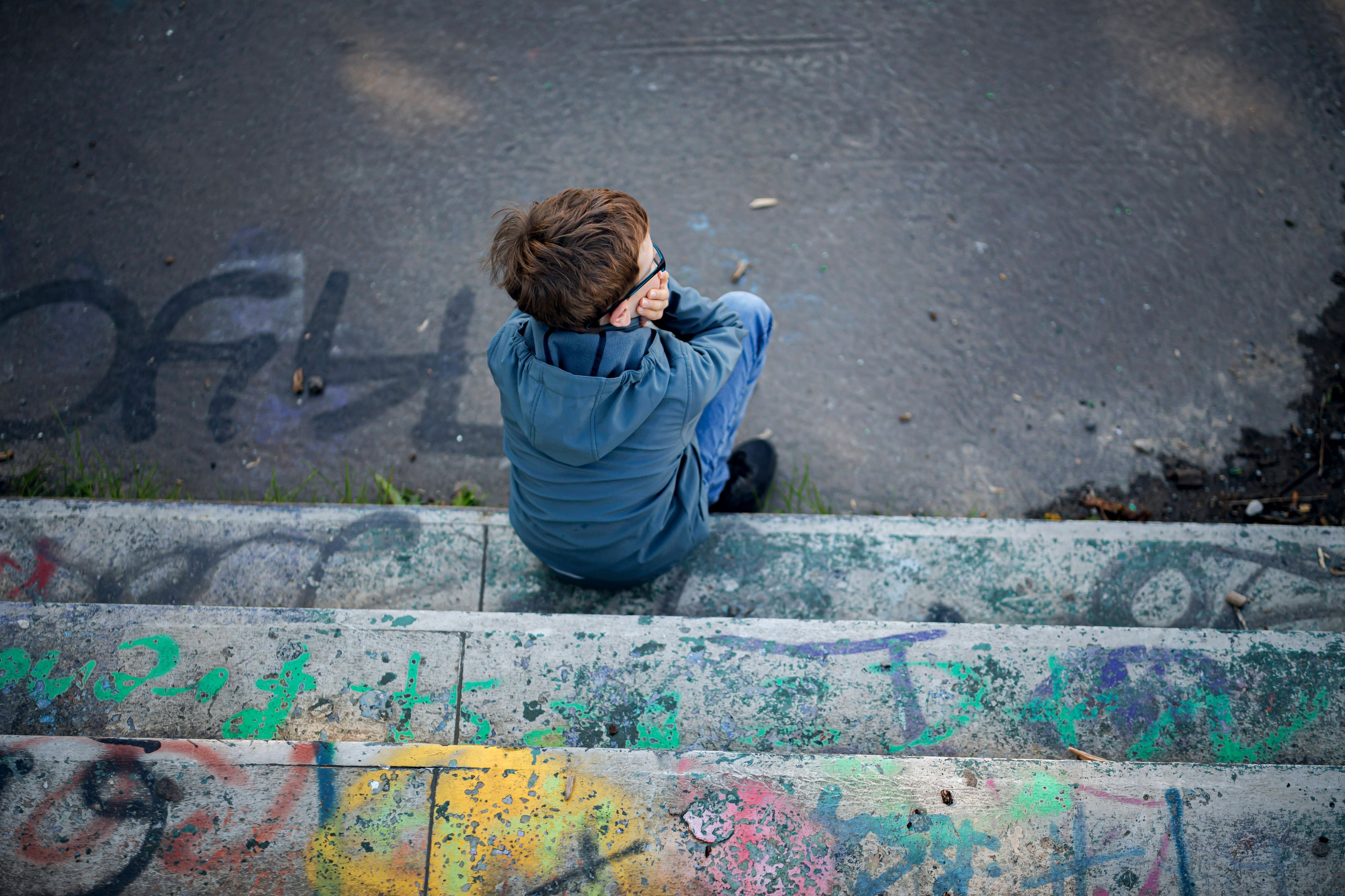 Ein Junge sitzt alleine auf einem mit Graffiti besprühten, heruntergekommenen Spielplatz.