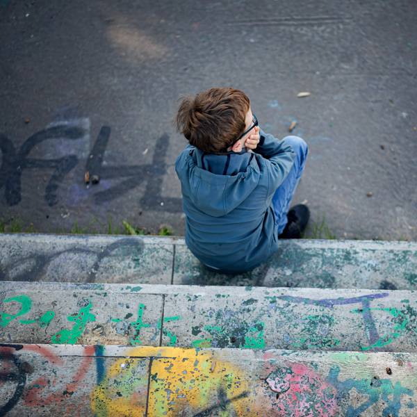 Ein Junge sitzt alleine auf einem mit Graffiti besprühten, heruntergekommenen Spielplatz.