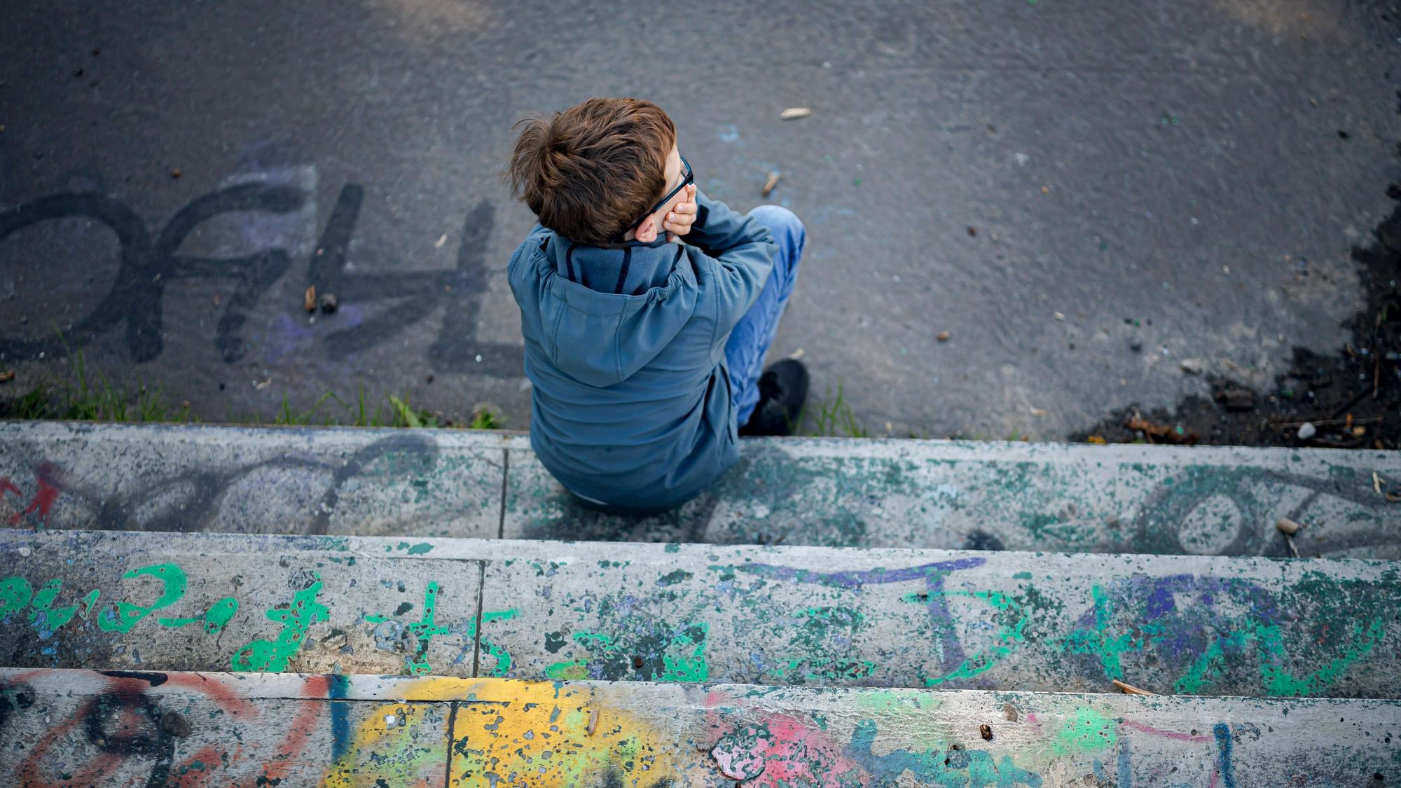 Ein Junge sitzt alleine auf einem mit Graffiti besprühten, heruntergekommenen Spielplatz.