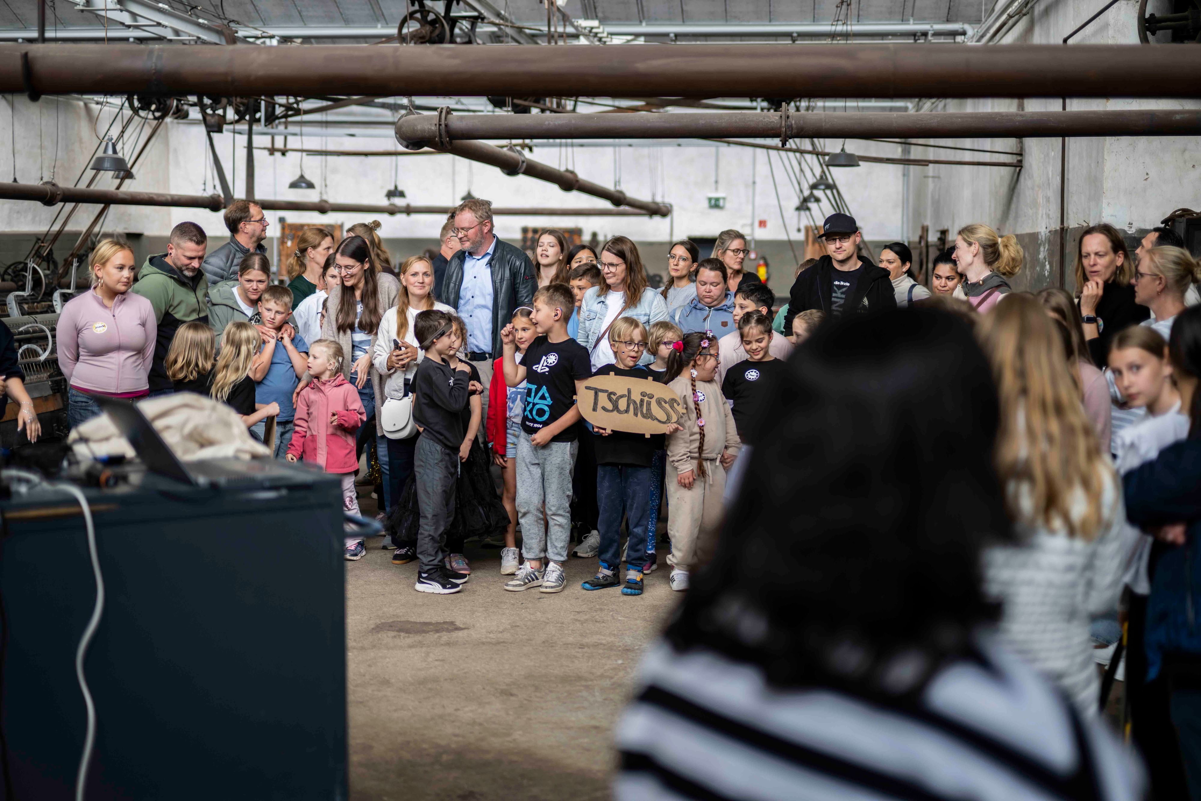 Eine Gruppe Kinder steht zusammen. Ein Kind hält ein Pappschild in der Hand, auf dem steht: „Tschüss“.