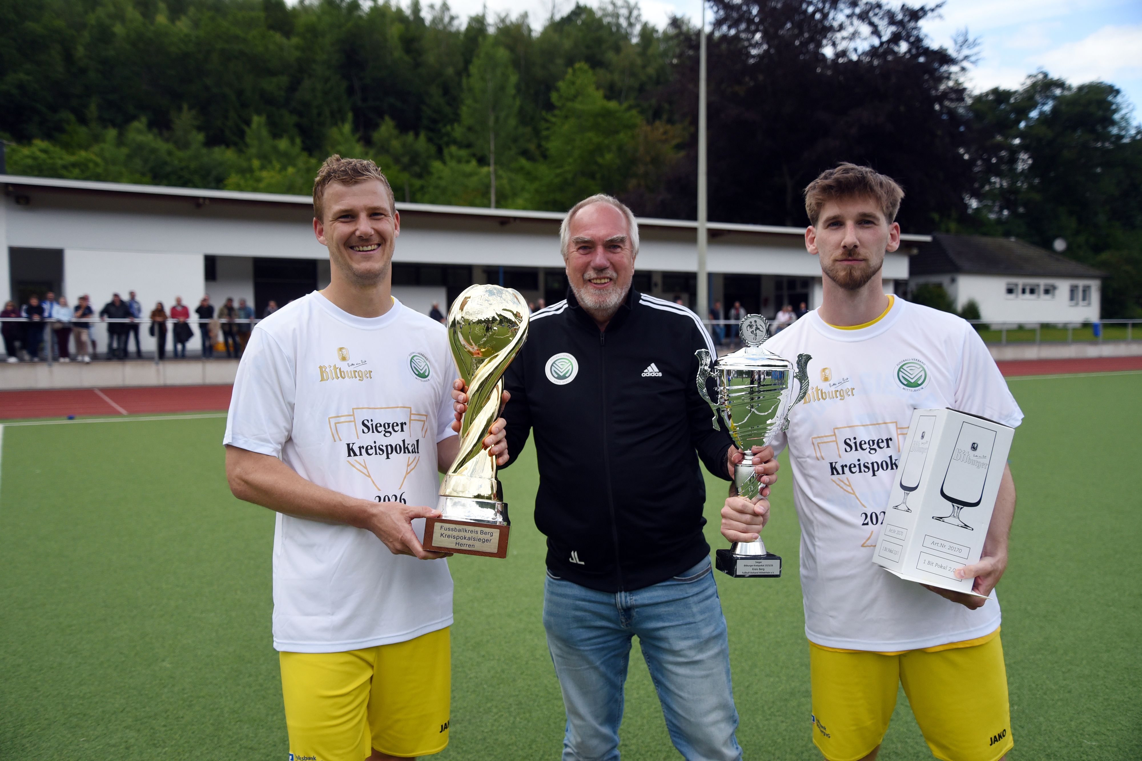 Pokalübergabe eines Offiziellen an zwei Fußballspieler