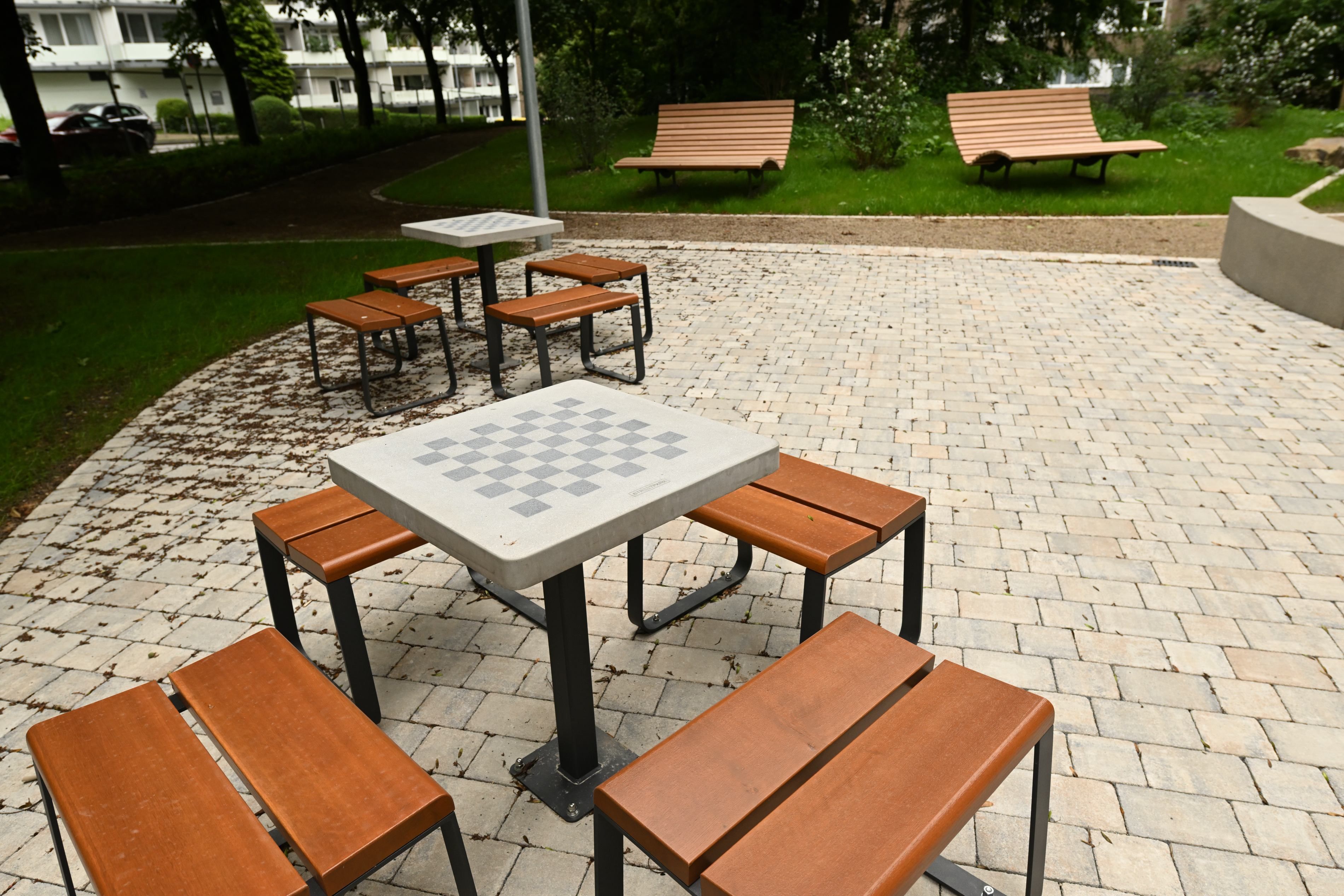 Im Park stehen Holzhocker um einen Tisch mit Schachbrett.