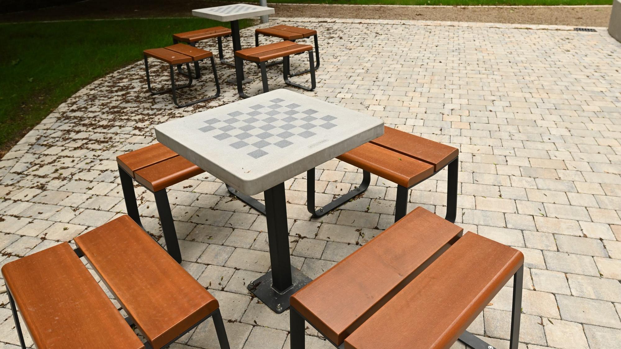 Im Park stehen Holzhocker um einen Tisch mit Schachbrett.