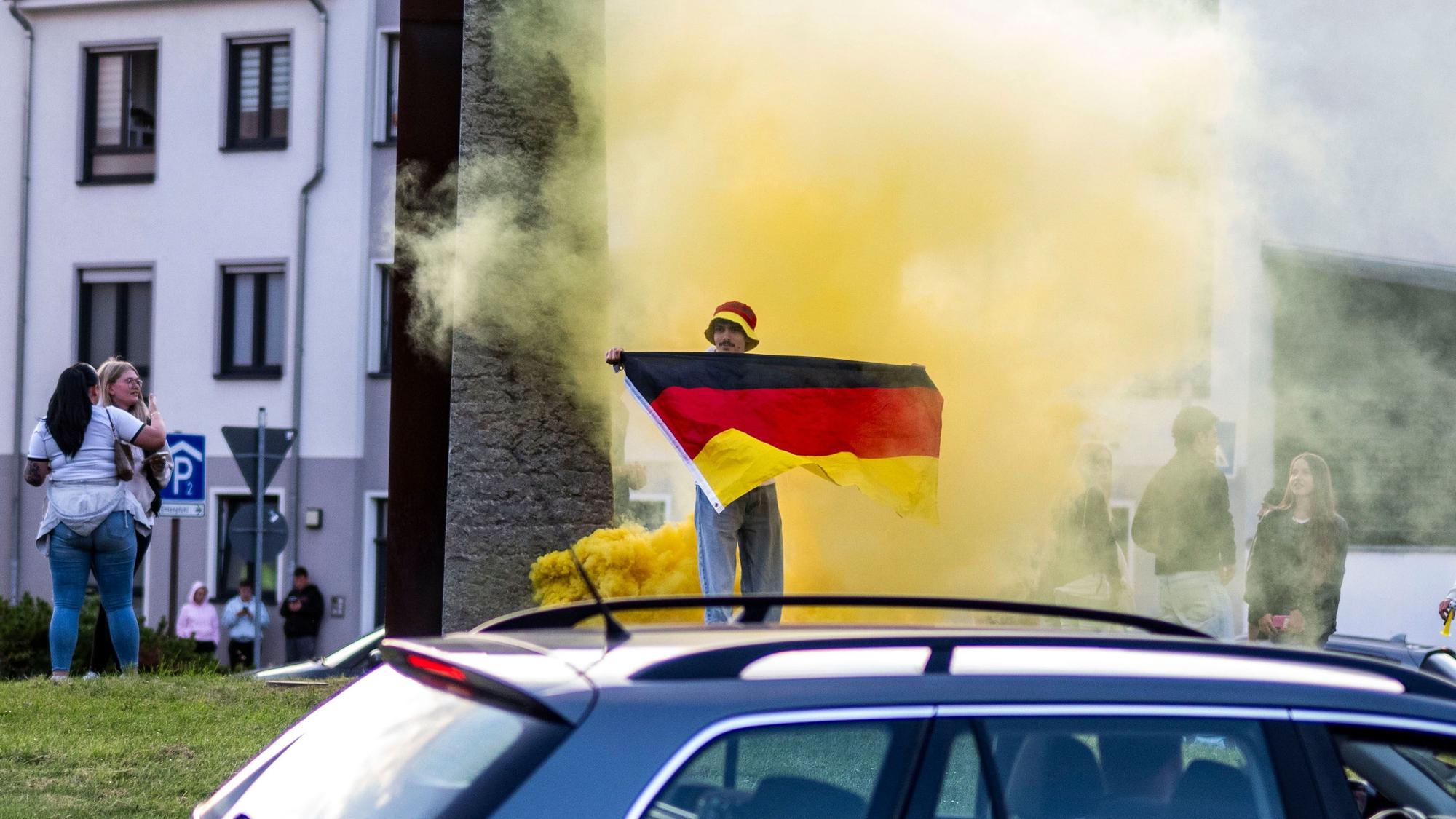 Ein Mann hält eine Deutschland-Fahne vor die Brust, im Hintergrund ist gelber Rauch zu erkennen.