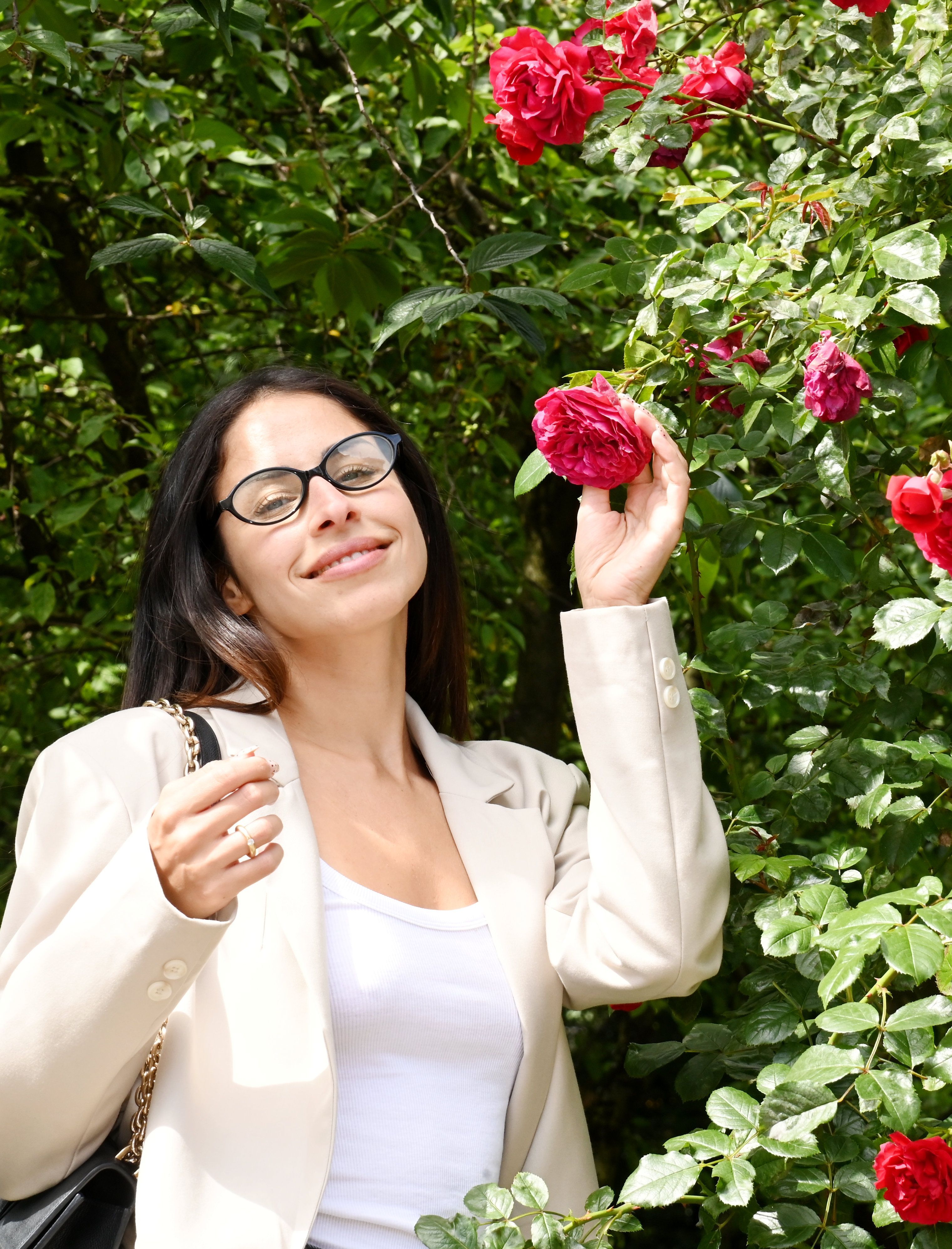Eine junge Frau mit dunklem Haar und Brille hält eine Rose in der Hand.