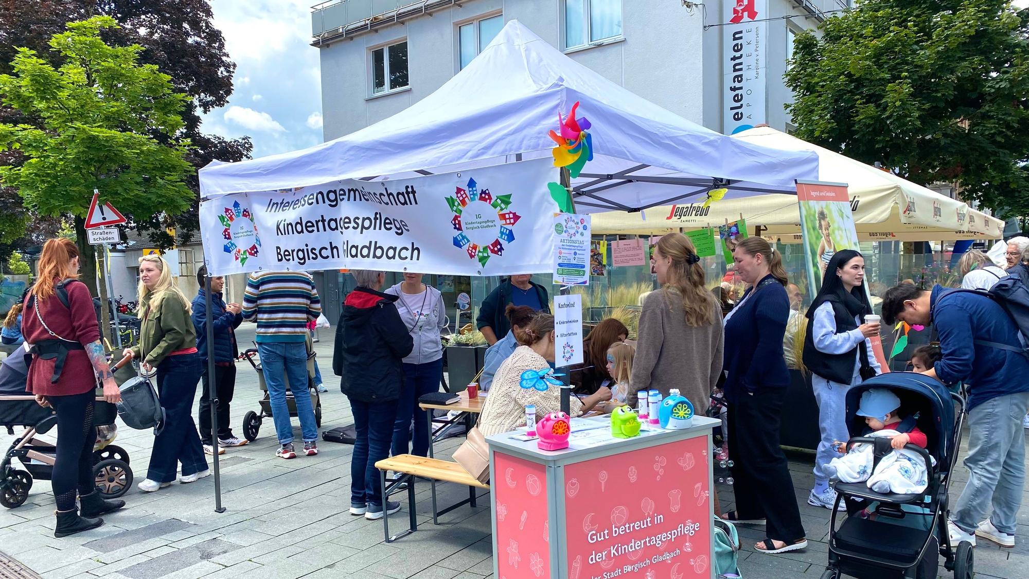Um den Stand der Tagesmütter stehen viele Personen und unterhalten sich.