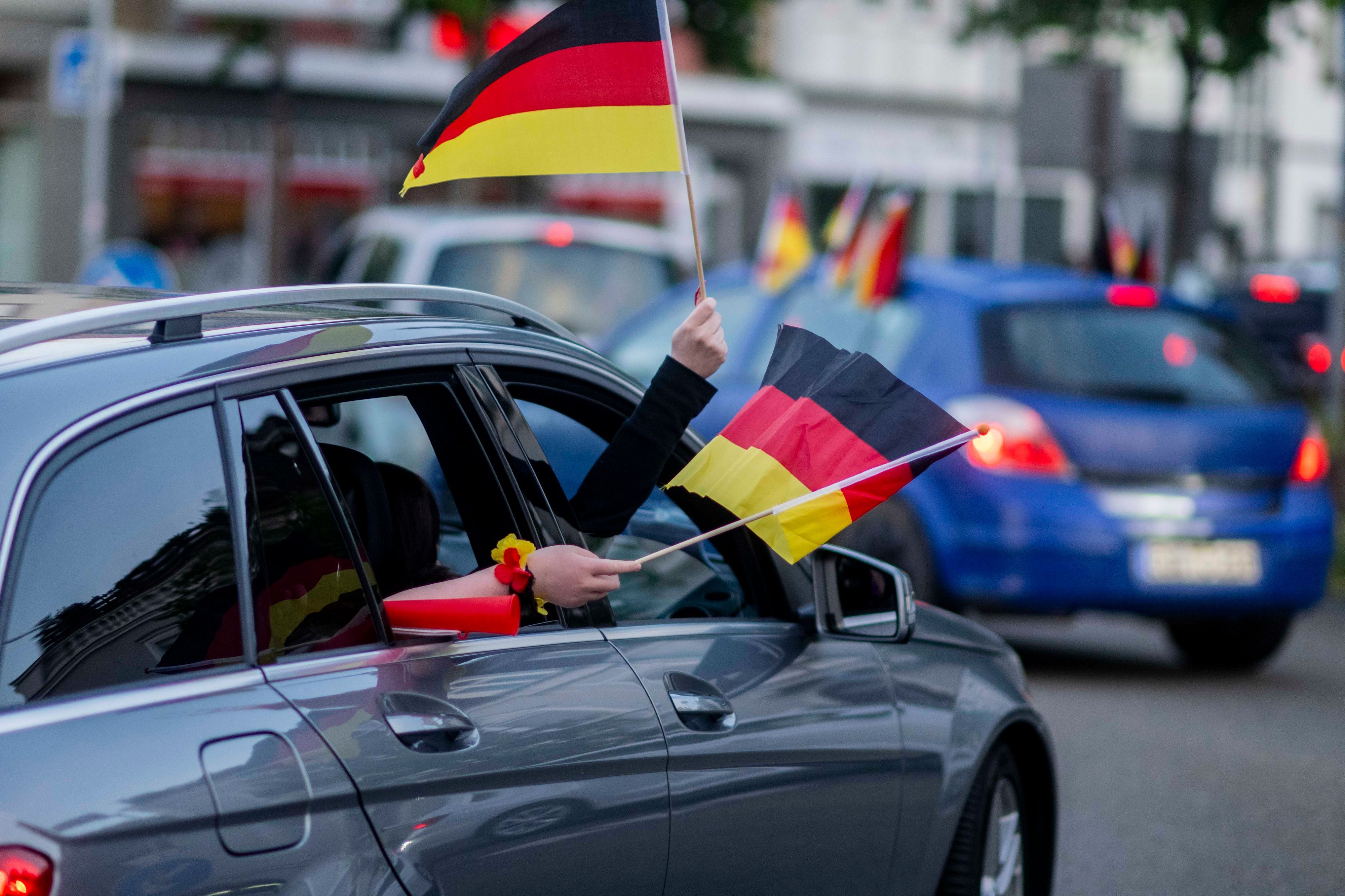 Aus einem Auto im Autokorso nach dem WM-Auftaktsieg wird mit zwei Deutschland-Fähnchen gewunken.