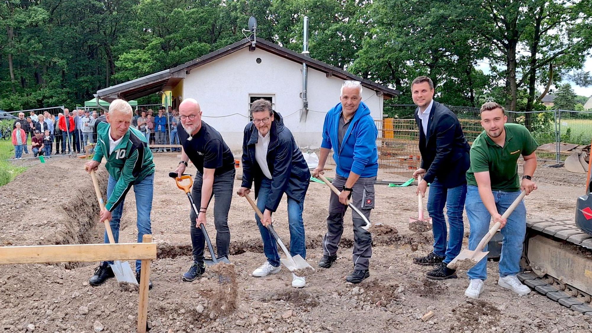 Die sechs Männer, die in einer Reihe stehen, werfen mit Spaten Erde in die Luft.