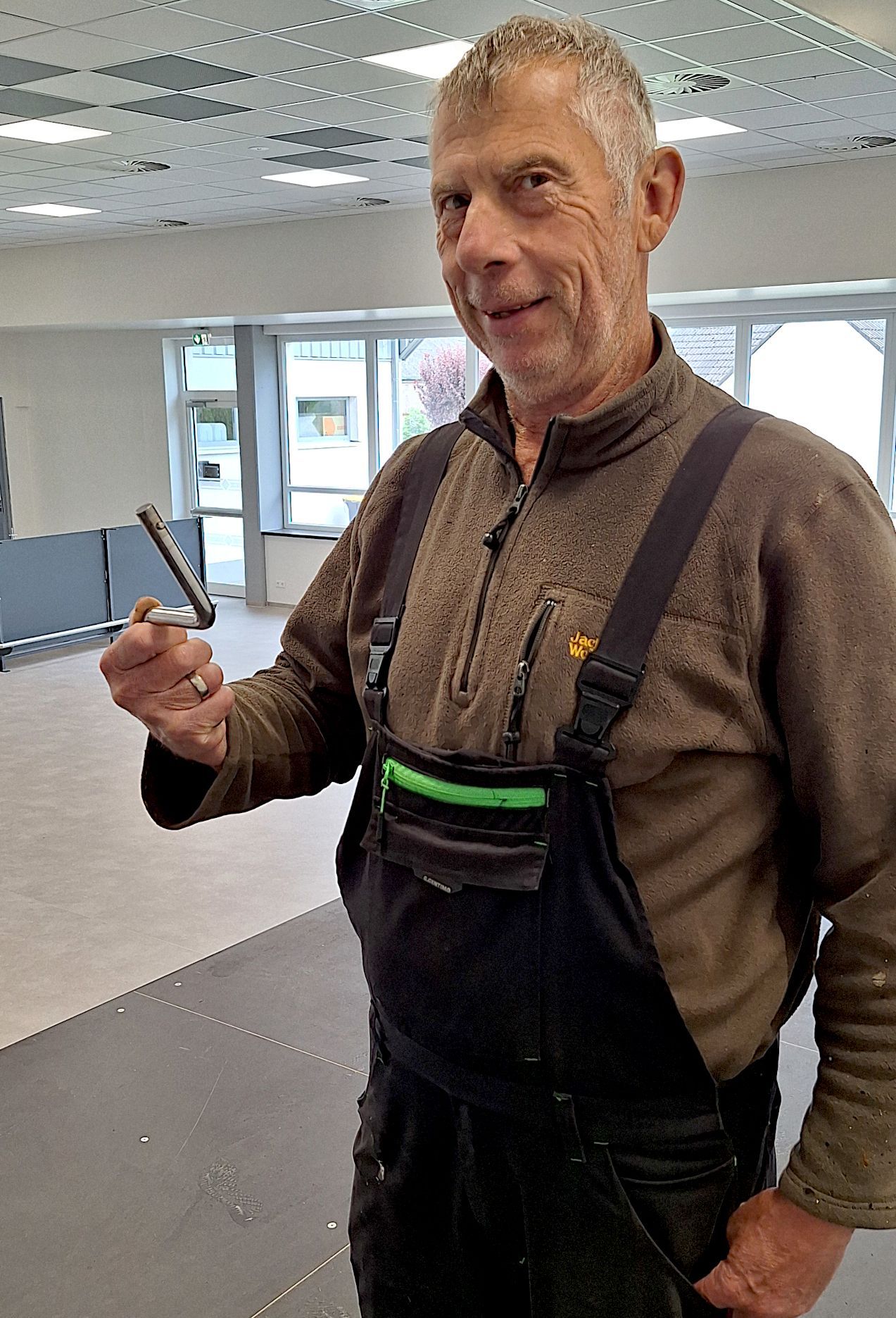 Ein Mann in Arbeitskleidung hält eine Kurbel in die Kamera.