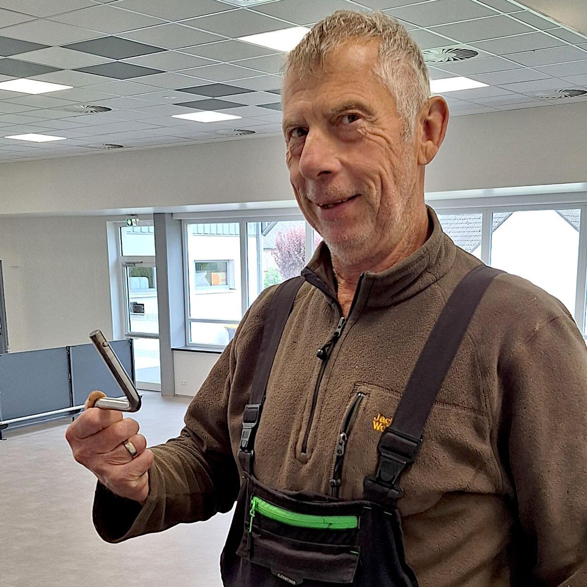 Ein Mann in Arbeitskleidung hält eine Kurbel in die Kamera.