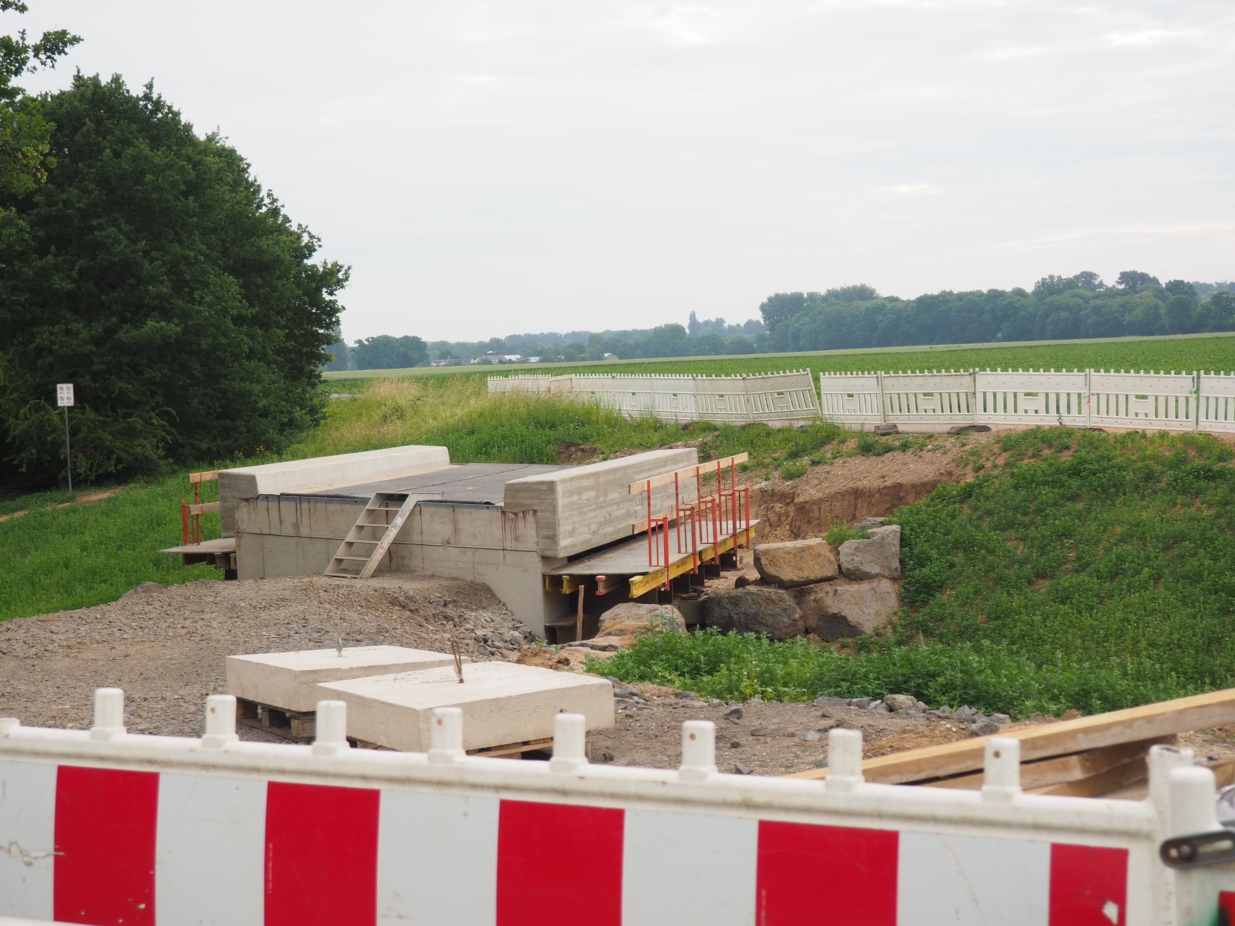 Hinter einer Absperrbake steht eine Brücke, die noch nicht an einen Weg angebunden ist.