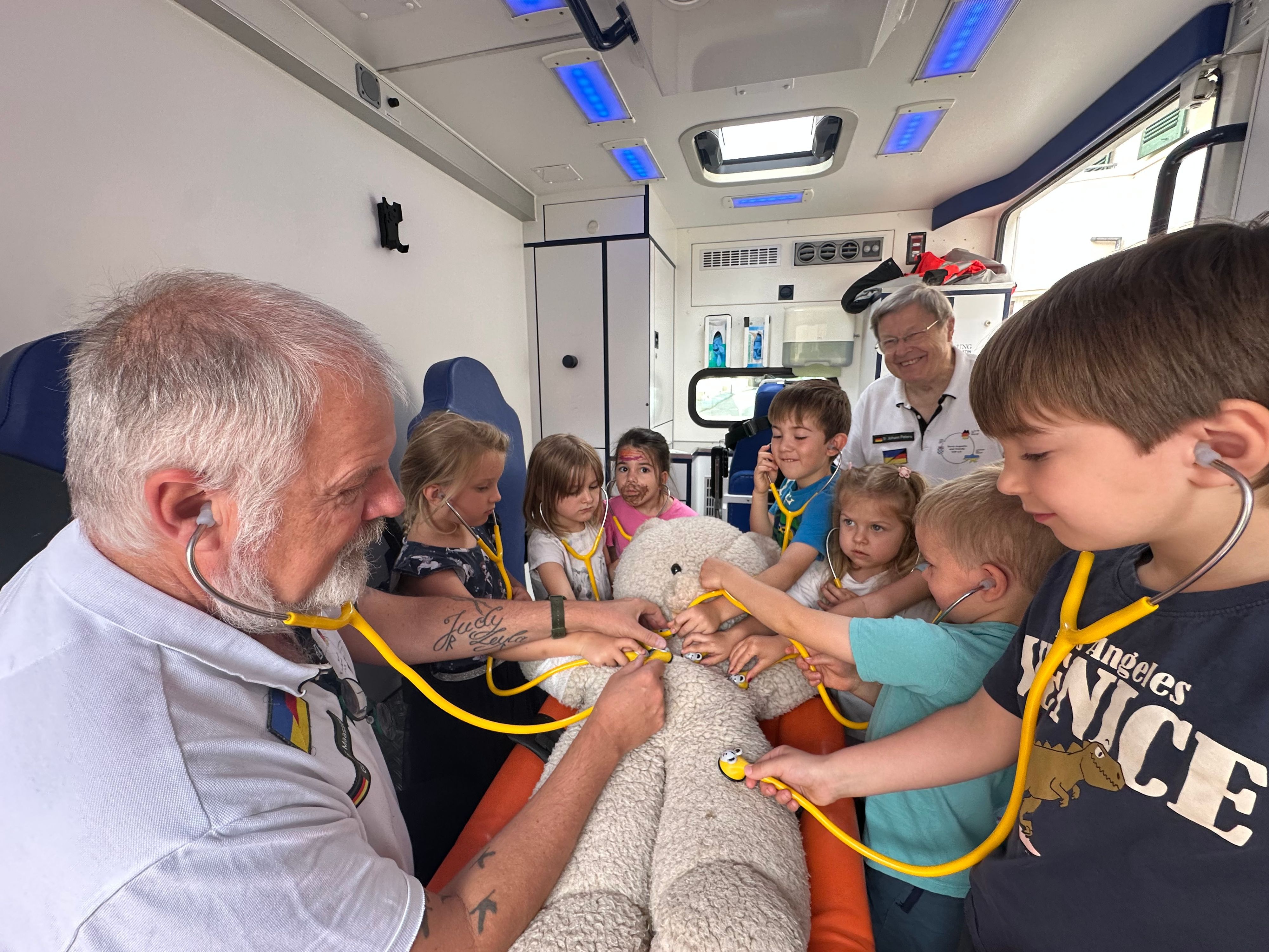 Der Verein Sankt Augustin hilft erklärt Kindern aus der Kita Bismarckplatz wie ein Rettungswagen funktioniert. Gunter Maassen (l.) erklärt die Funktionsweise eines  Stethoskops.